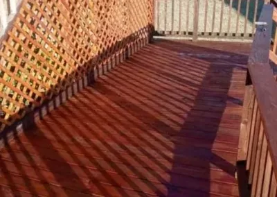 A wooden deck with a lattice fence and a nearby gate, cast with shadow patterns from the fencing.