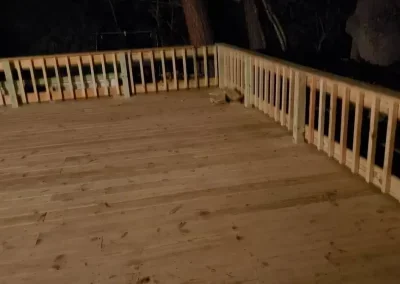 Empty wooden deck with a railing at night.