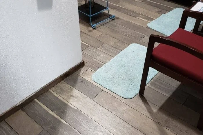 A corner of a room with hardwood floors, a white wall, a red upholstered chair with wooden arms, and two light blue rugs.