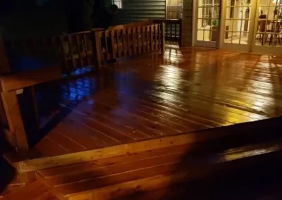 A polished wooden outdoor deck with bench seating, illuminated by warm lighting at night.