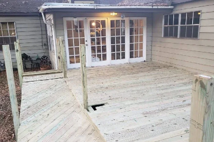 Newly built wooden deck outside a house with a glass door and windows, with some support posts in place but no railing.