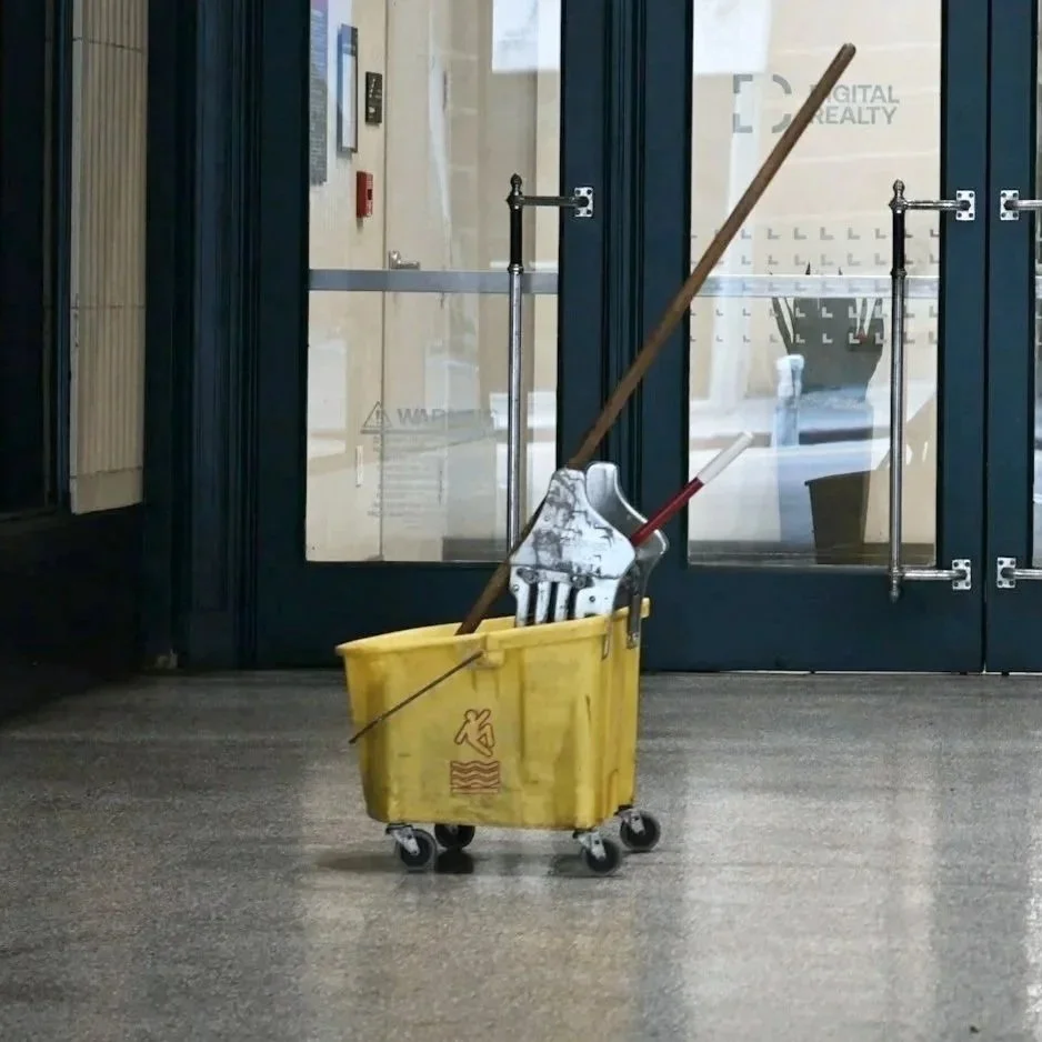 A person wearing yellow gloves cleaning a surface with a blue scrub brush, creating foam and bubbles in a close-up view.