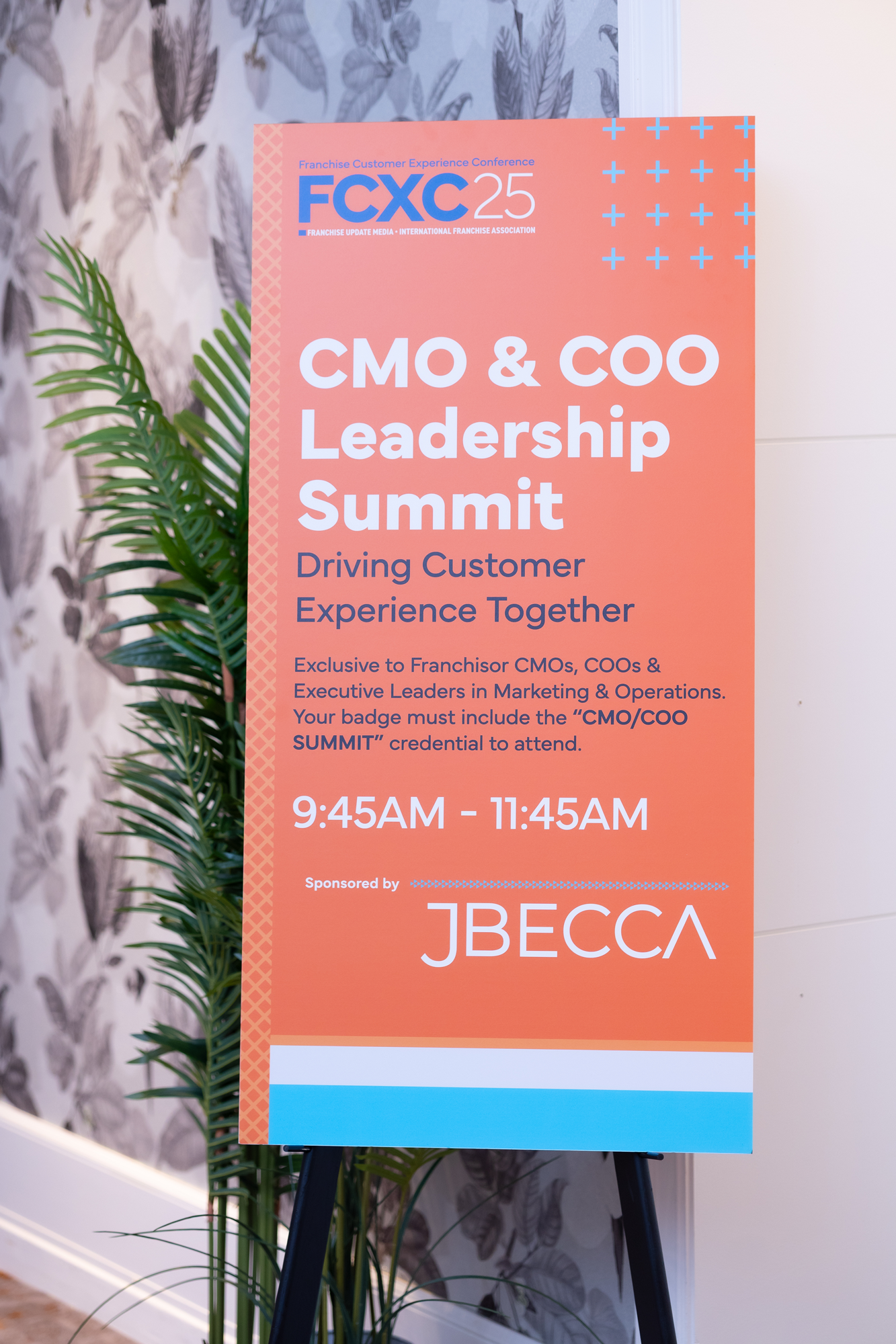 Sign for the CMO & COO Leadership Summit, part of the Franchise Customer Experience Conference, scheduled from 9:45AM to 11:45AM, sponsored by JBECCA, with a decorative leafy background.