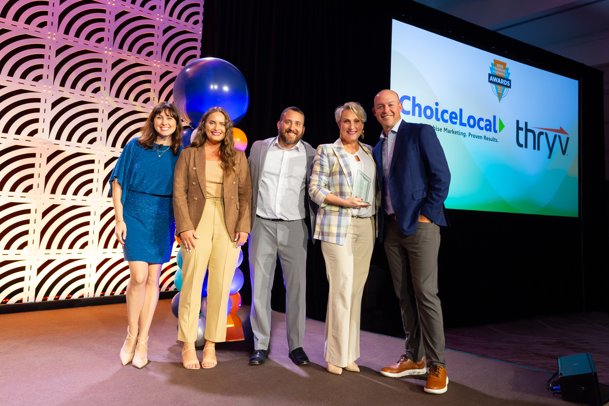 A group of five people standing on stage at an awards ceremony, smiling for a photo, with a large screen displaying logos for ChoiceLocal and Thryv in the background.
