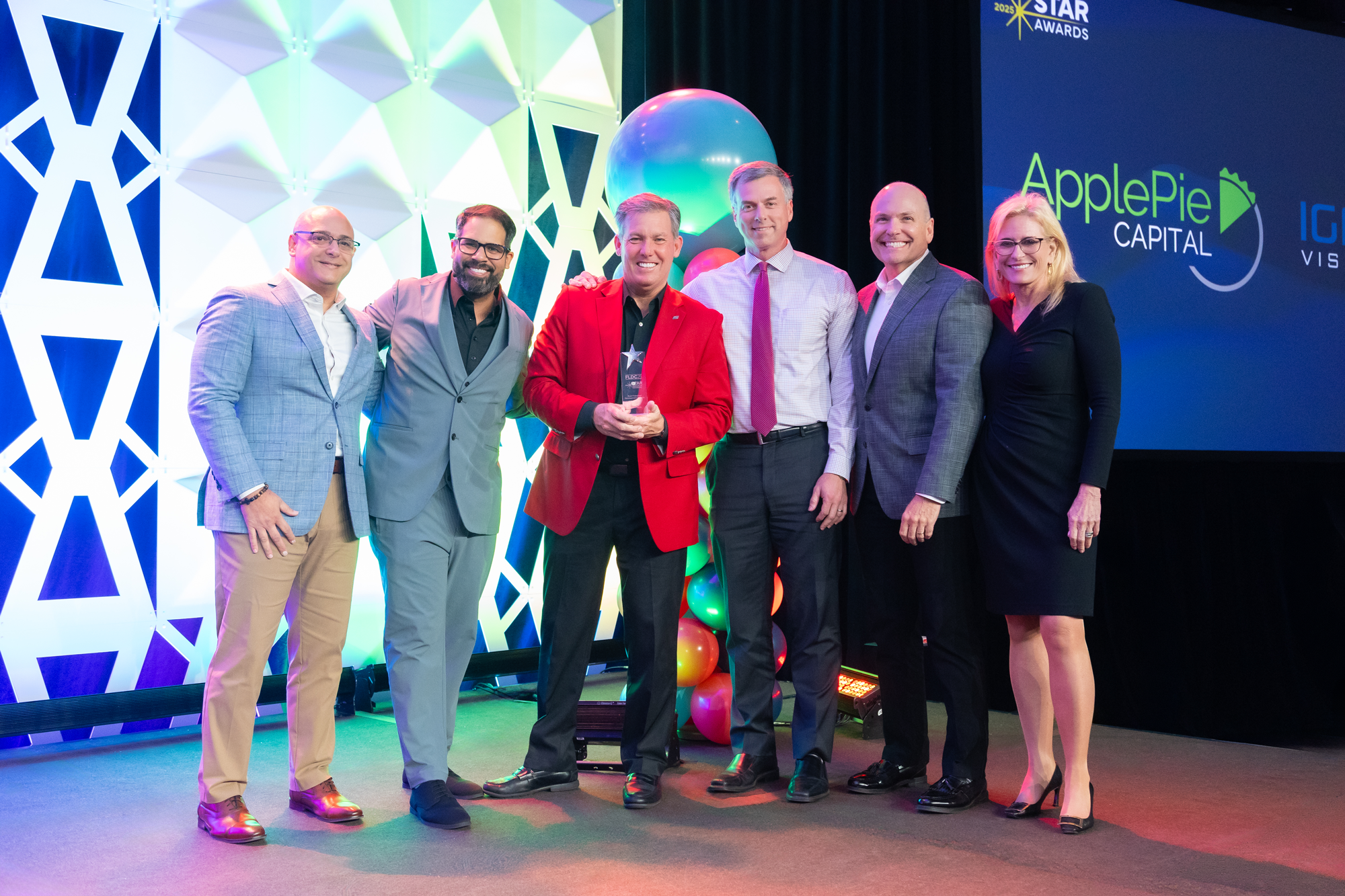Group of six people standing on stage with colorful balloons and a large screen displaying 'ApplePie Capital' and 'Star Awards' in the background, at an awards ceremony.