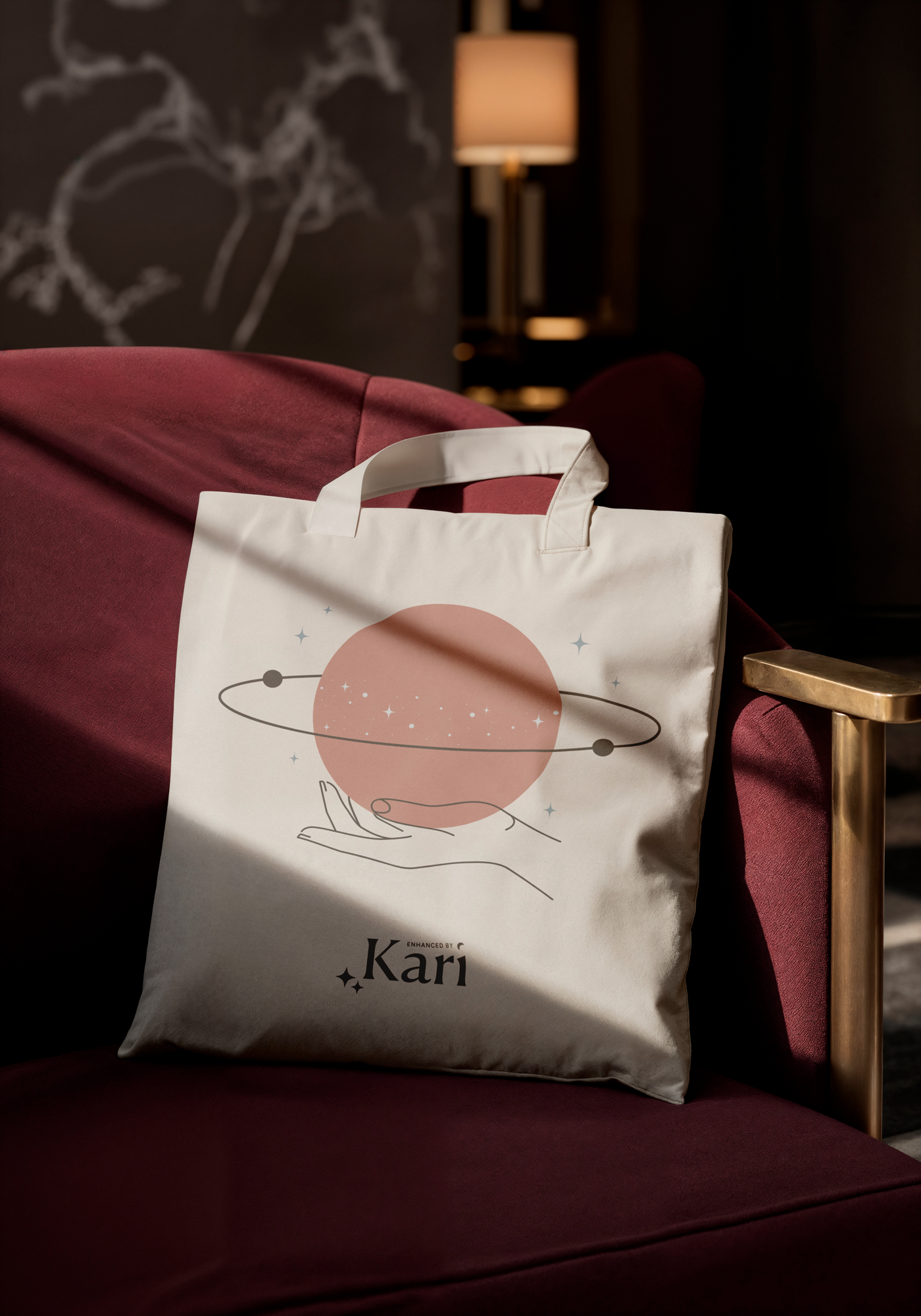 A white tote bag with a space-themed design featuring a planet and stars, with the name 'Kari' printed on it, resting on a red velvet armchair in a dimly lit room.