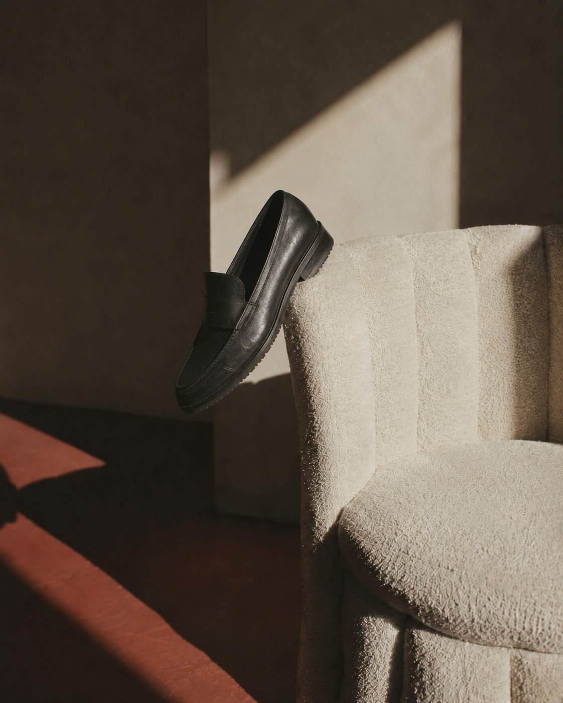 black leather loafer on beige upholstered chair 
with shadows and sunlight, hero image for 
Storytotellers creative consultancy