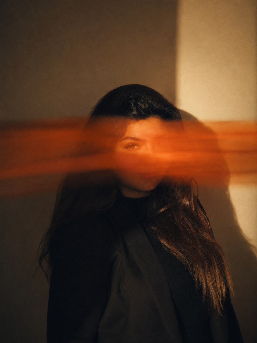 woman in black jacket against a wall with 
horizontal orange light streak across her face, 
editorial portrait for Storytotellers