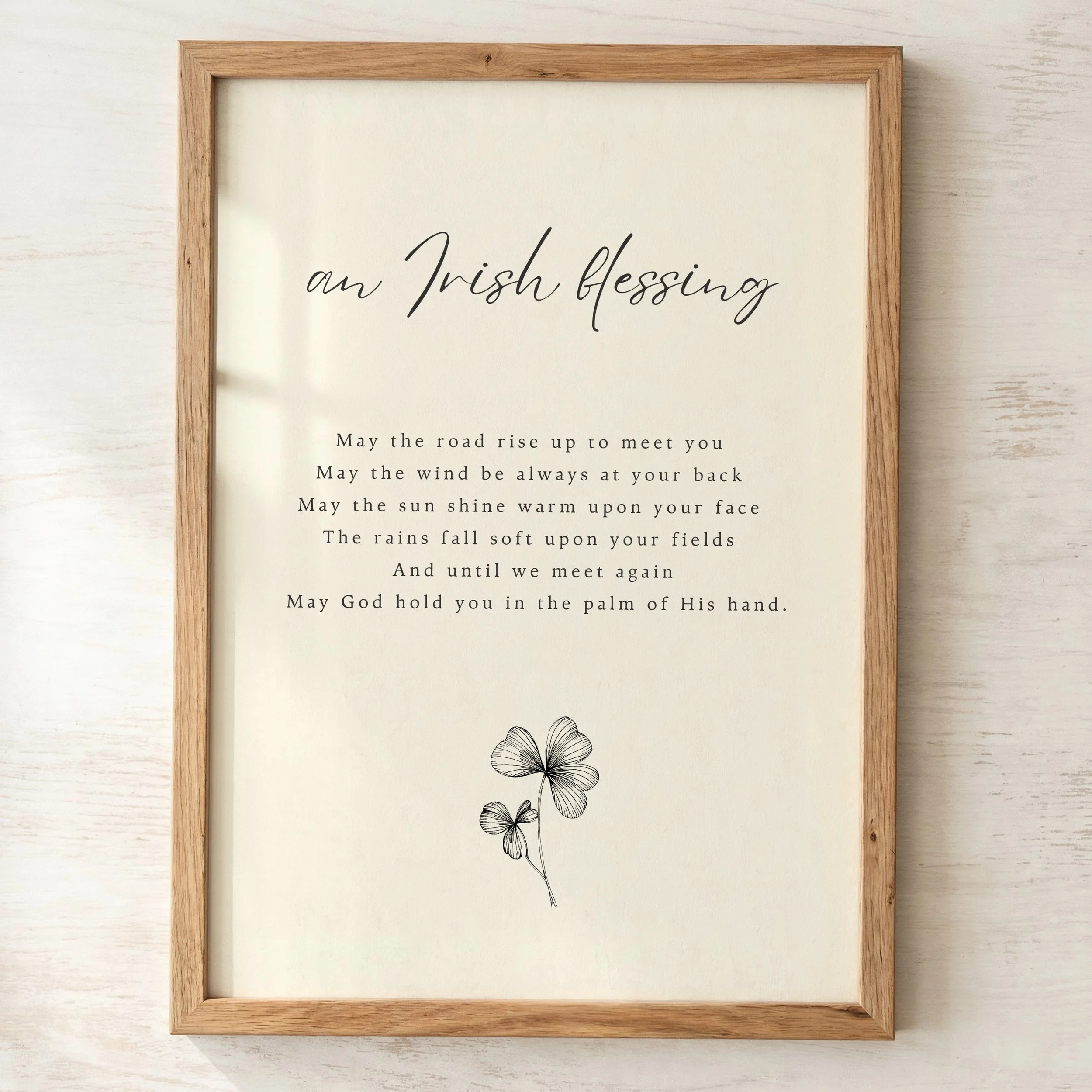 A framed print with a wooden border displaying a blessing in black cursive text and a black and white illustration of three flowers at the bottom, on a textured white background.