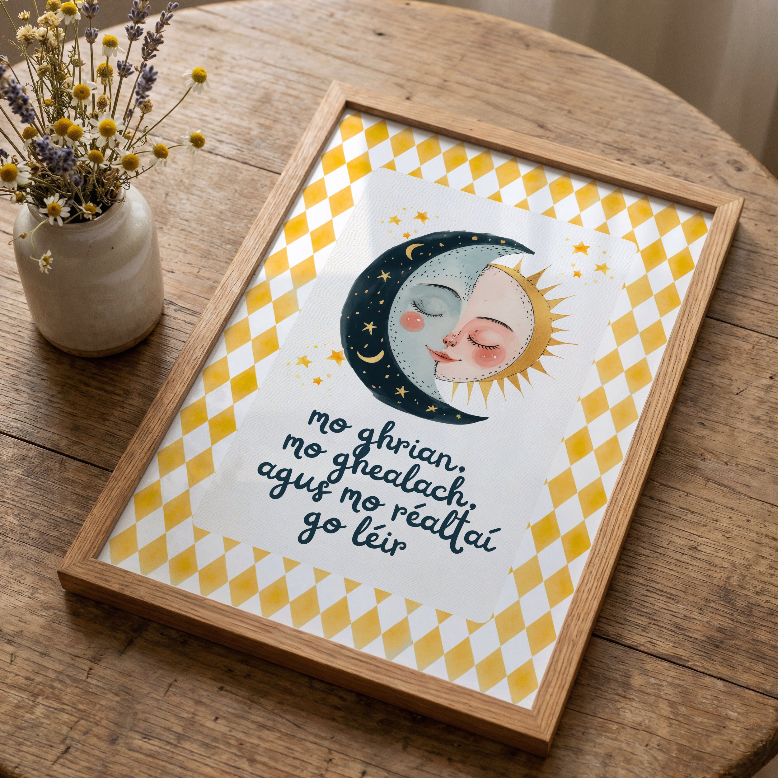 A wooden table with a vase of daisies and lavender flowers on the left, and a framed illustrated cloth showing a celestial-themed face with sun, moon, and stars on the right. Irish Language nursery Print
