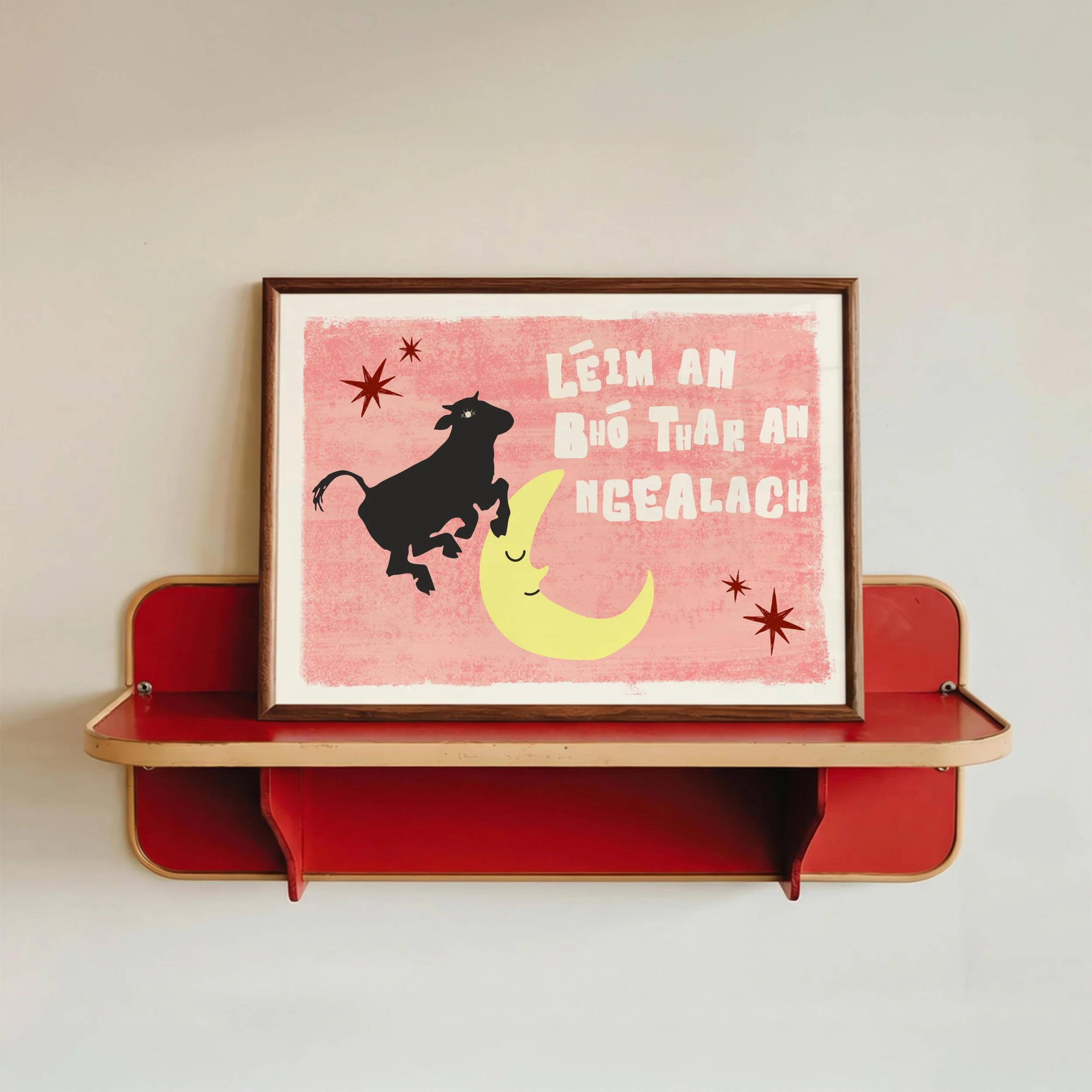 Red and beige cushioned bench with a framed print leaning against the wall above it. The print has a pink background, black animal silhouette, moon, and stars with Vietnamese text.