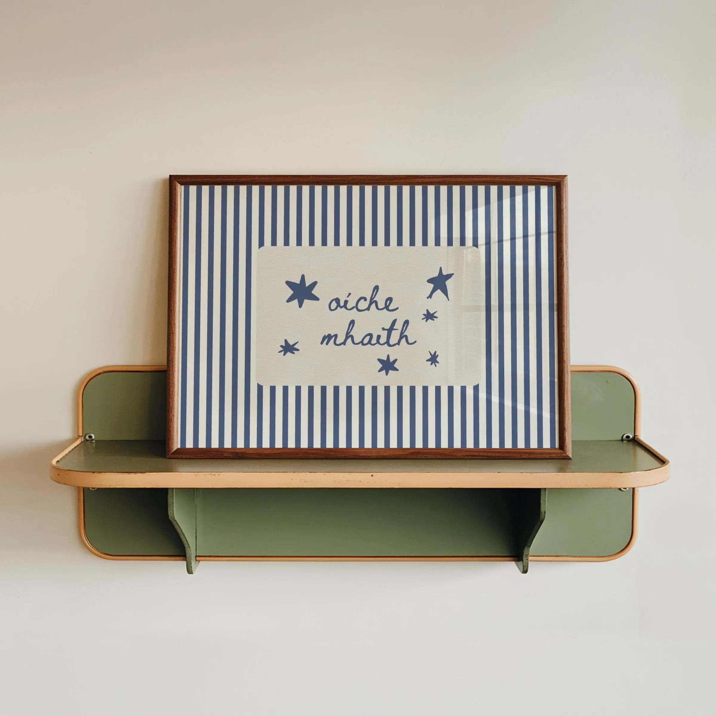 Decorative framed print on a plain wall with the words 'aíche a chraiceann' surrounded by star illustrations, with a small shelf below holding multicolored panels.  Irish Language nursery Print