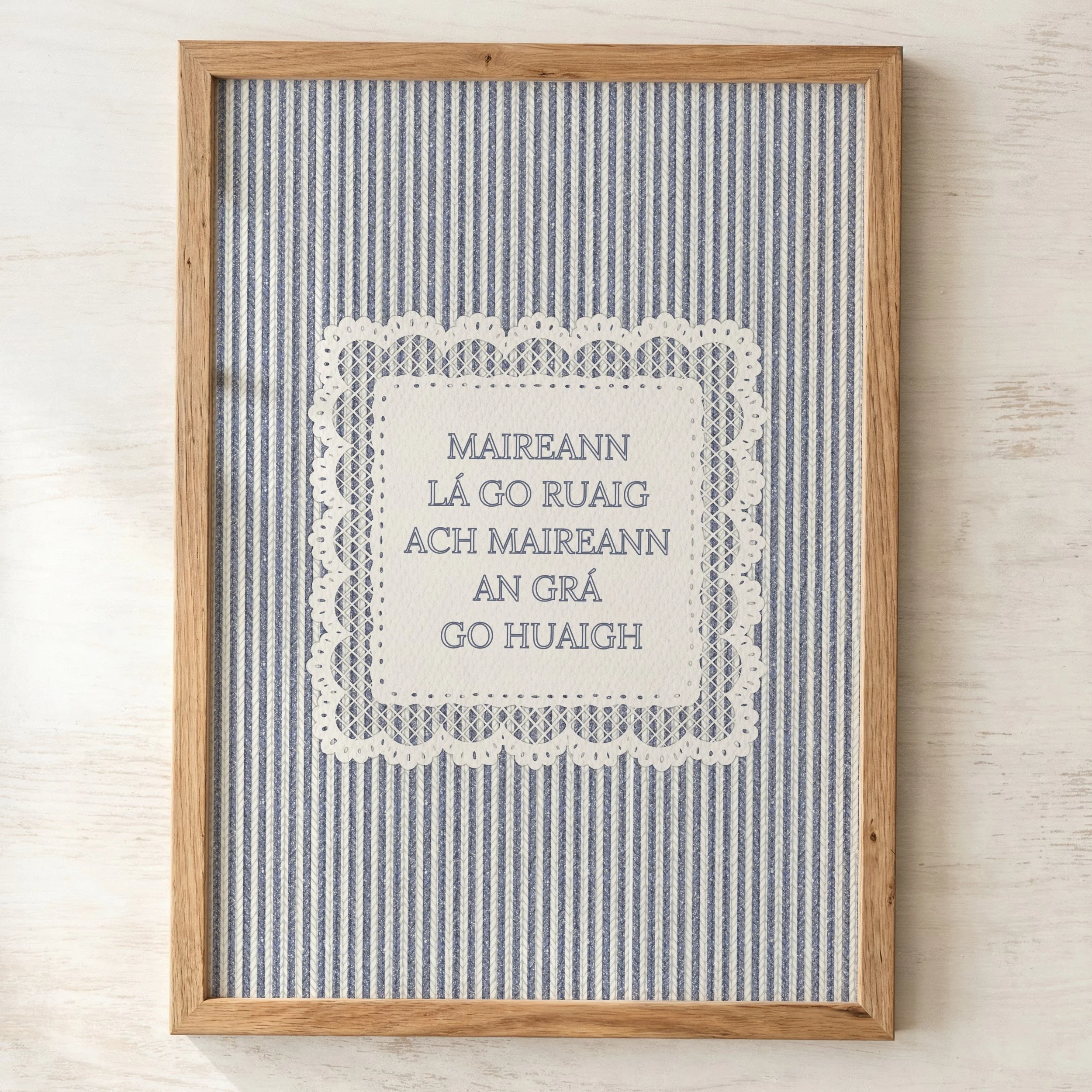 A framed art piece with a blue and white striped background, and a decorative white paper cutout in the center with Irish names and words. Gaeilge romantic quote
