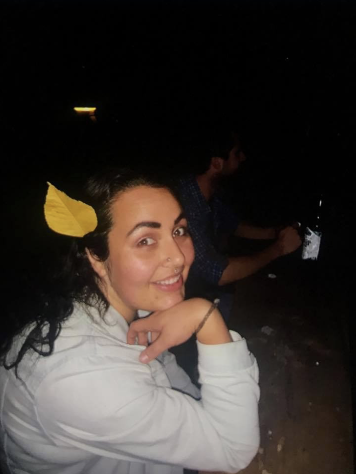 A woman with dark hair and a yellow hair accessory smiling at the camera, sitting at a table in a dark environment.