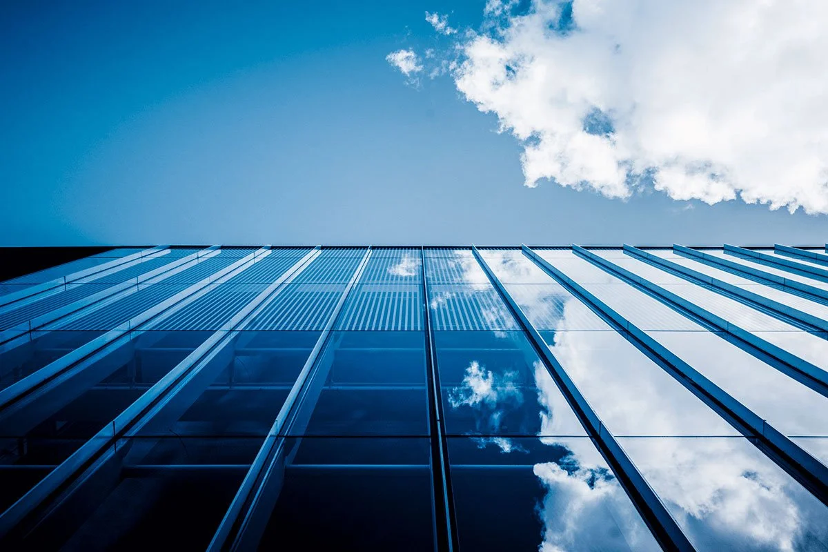 Low-angle view of a modern glass skyscraper reflecting the cloudy sky.