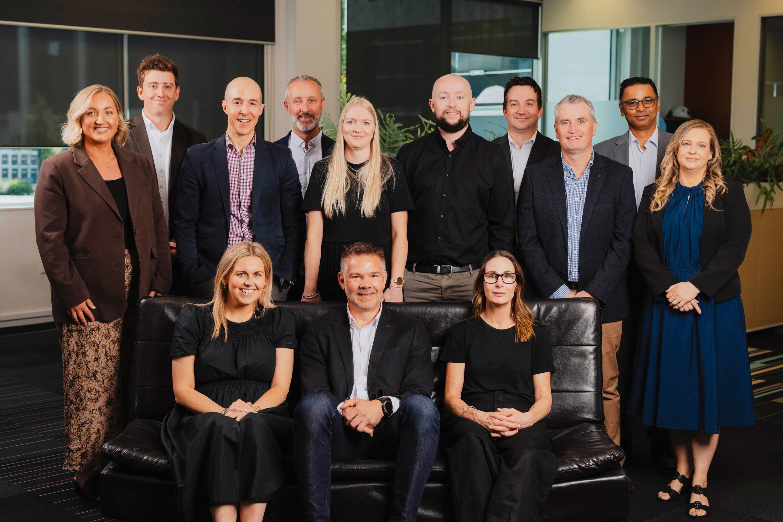 Group of eleven diverse professionals in business attire posing together in an indoor office setting.