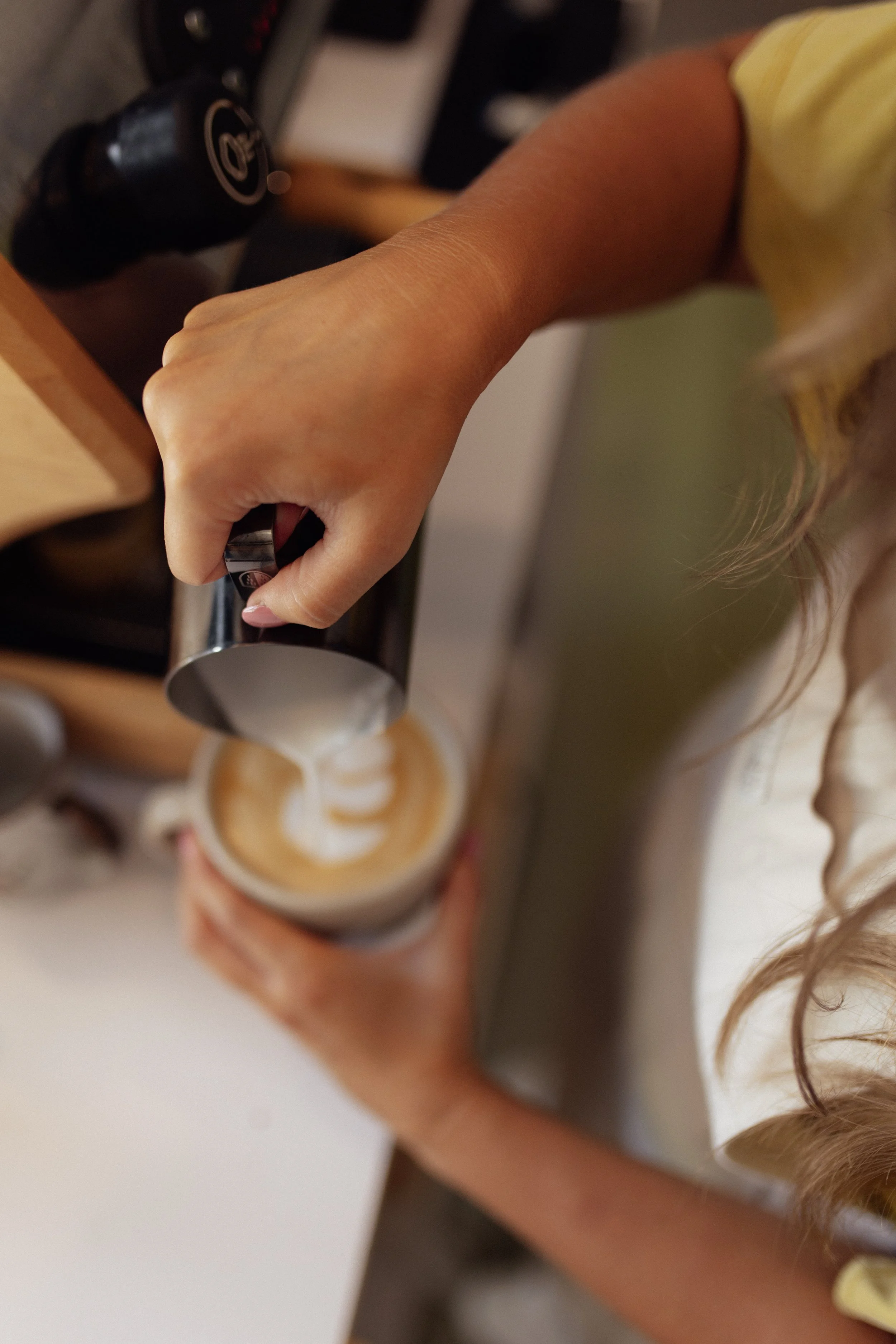 Person pouring milk into a cup of coffee with latte art on top.