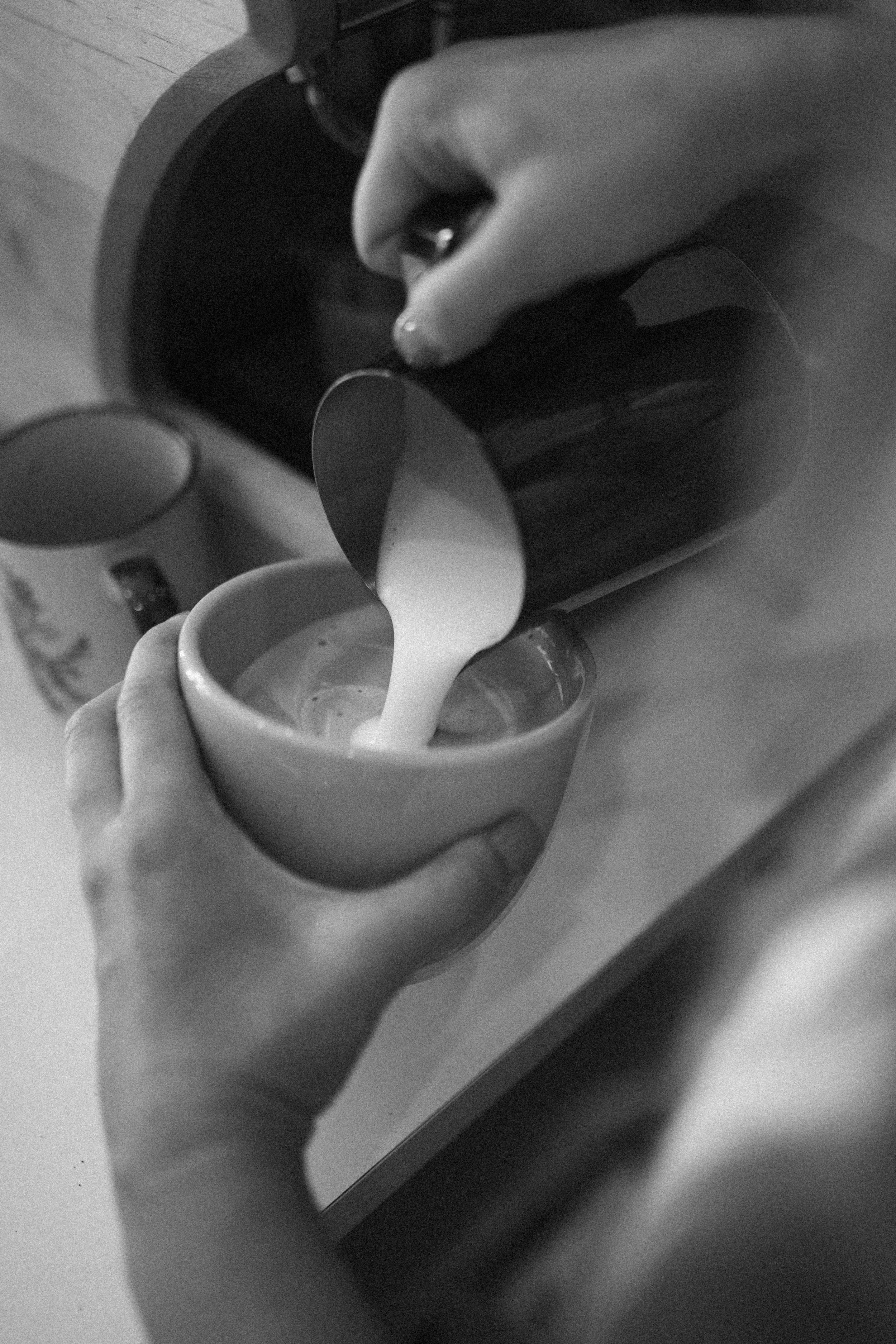 A person holding a small mug under a coffee dripper with hot water, preparing pour-over coffee in a black and white photo.