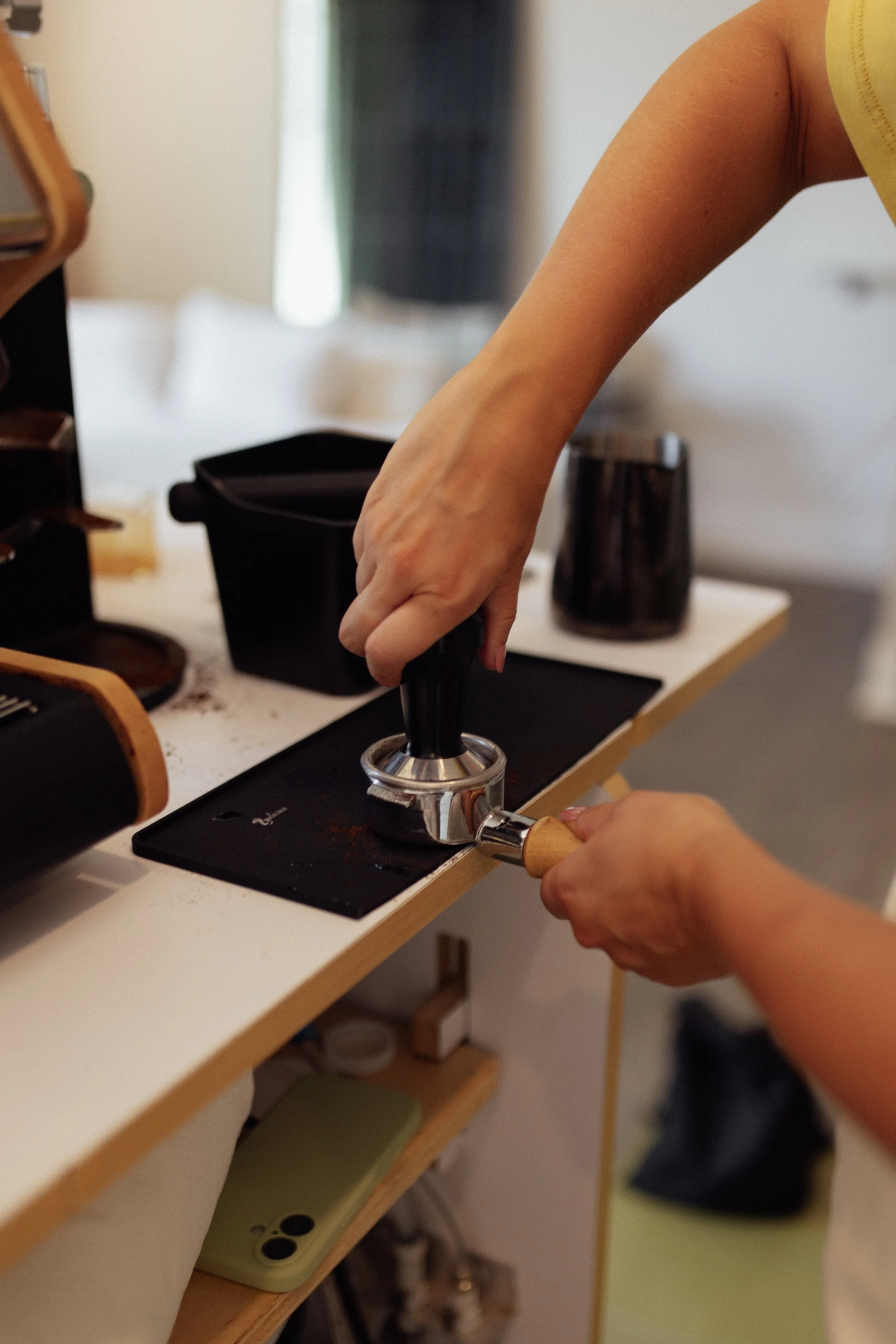 A person pressing a tamper on ground coffee in a coffee press machine at a coffee station.