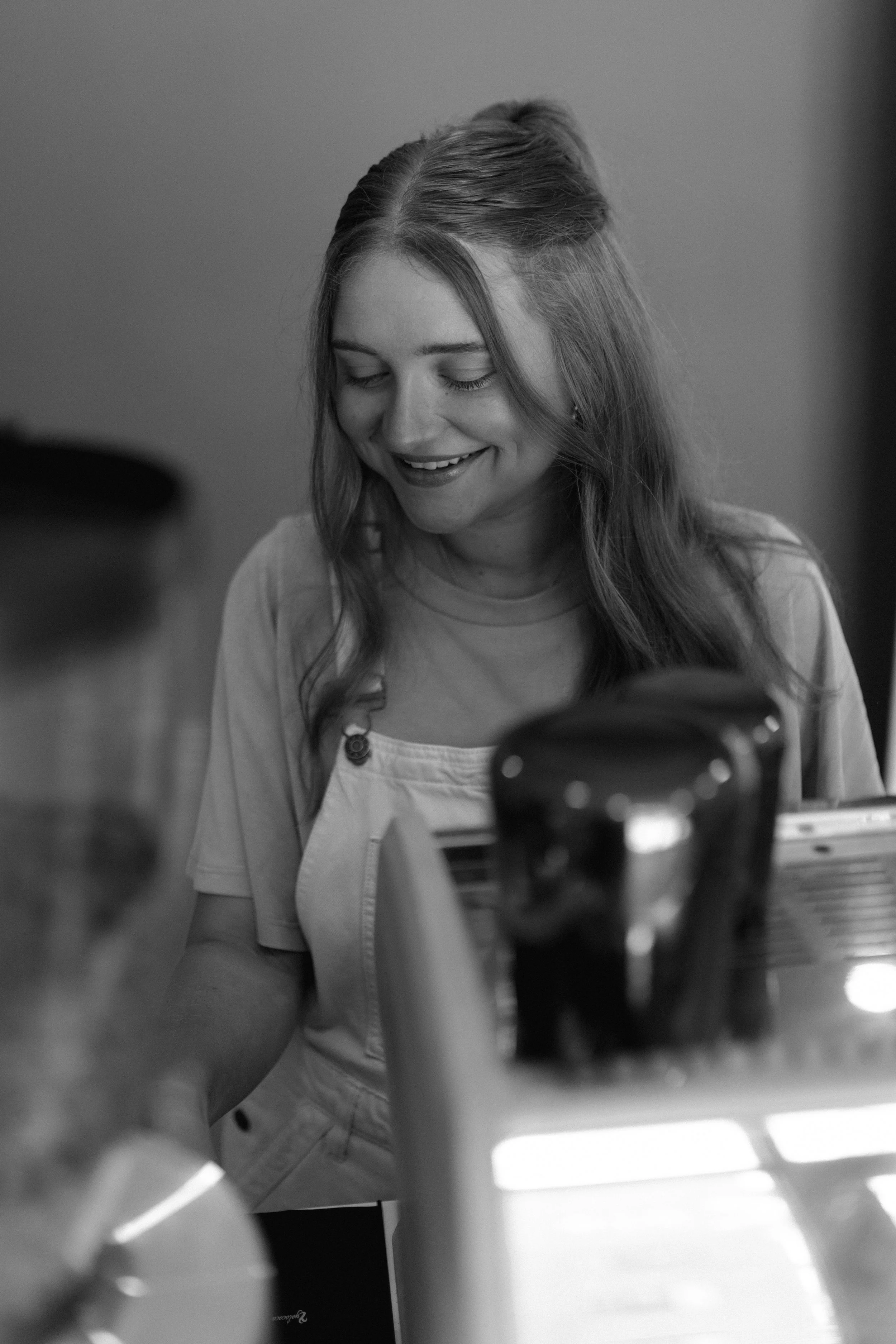 A black and white photo of a smiling woman with long hair looking down at a table with condiments and bottles.