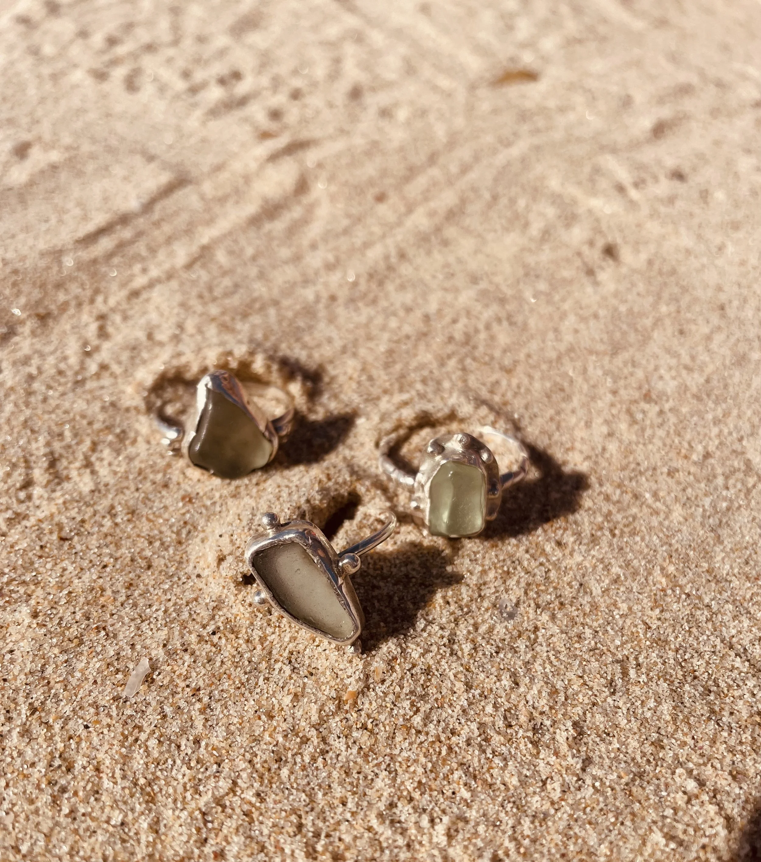 Close-up of several decorative rings on a sandy surface with small shells scattered around.