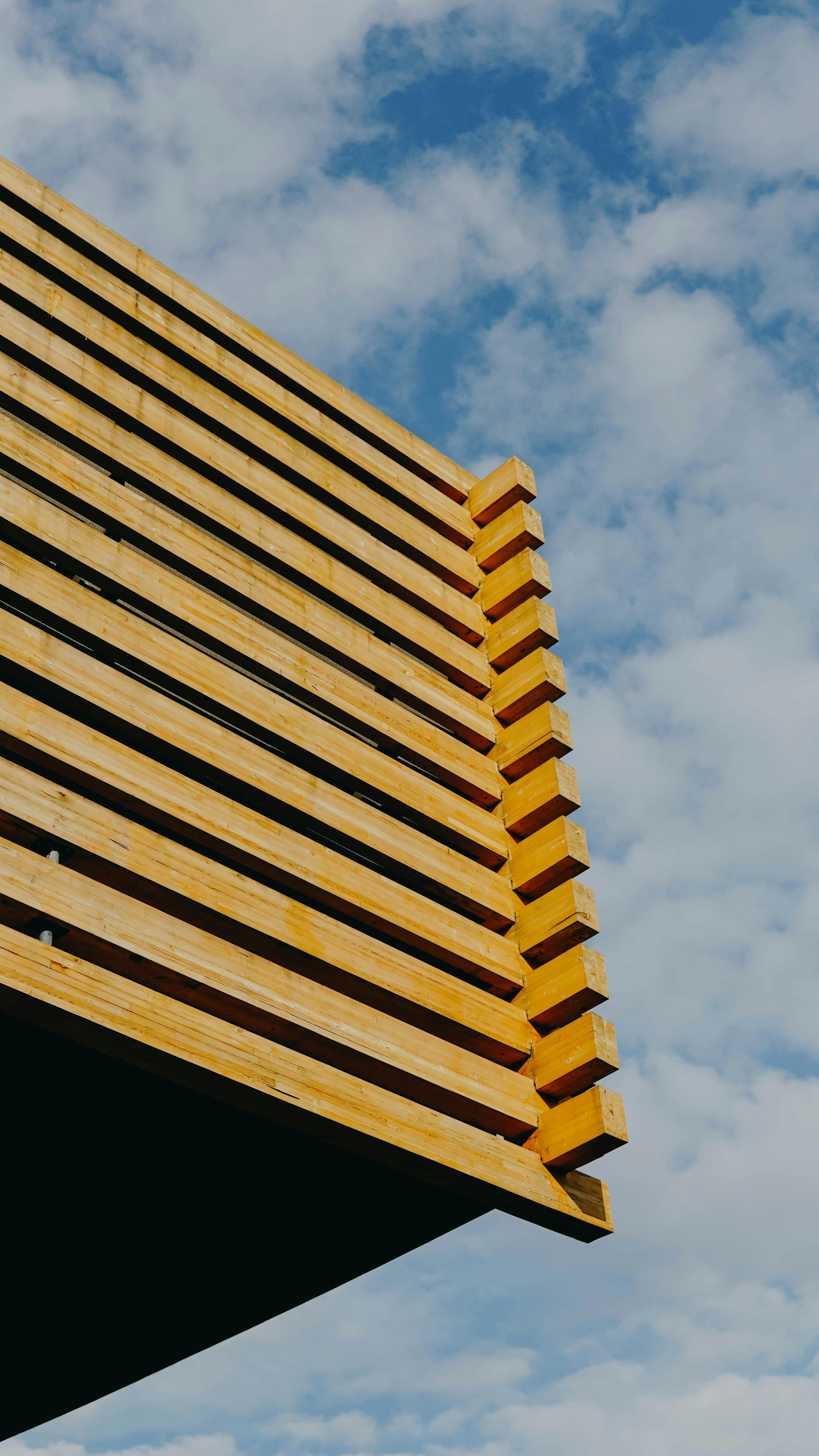 Close-up of a modern wooden architectural structure against a partly cloudy sky.