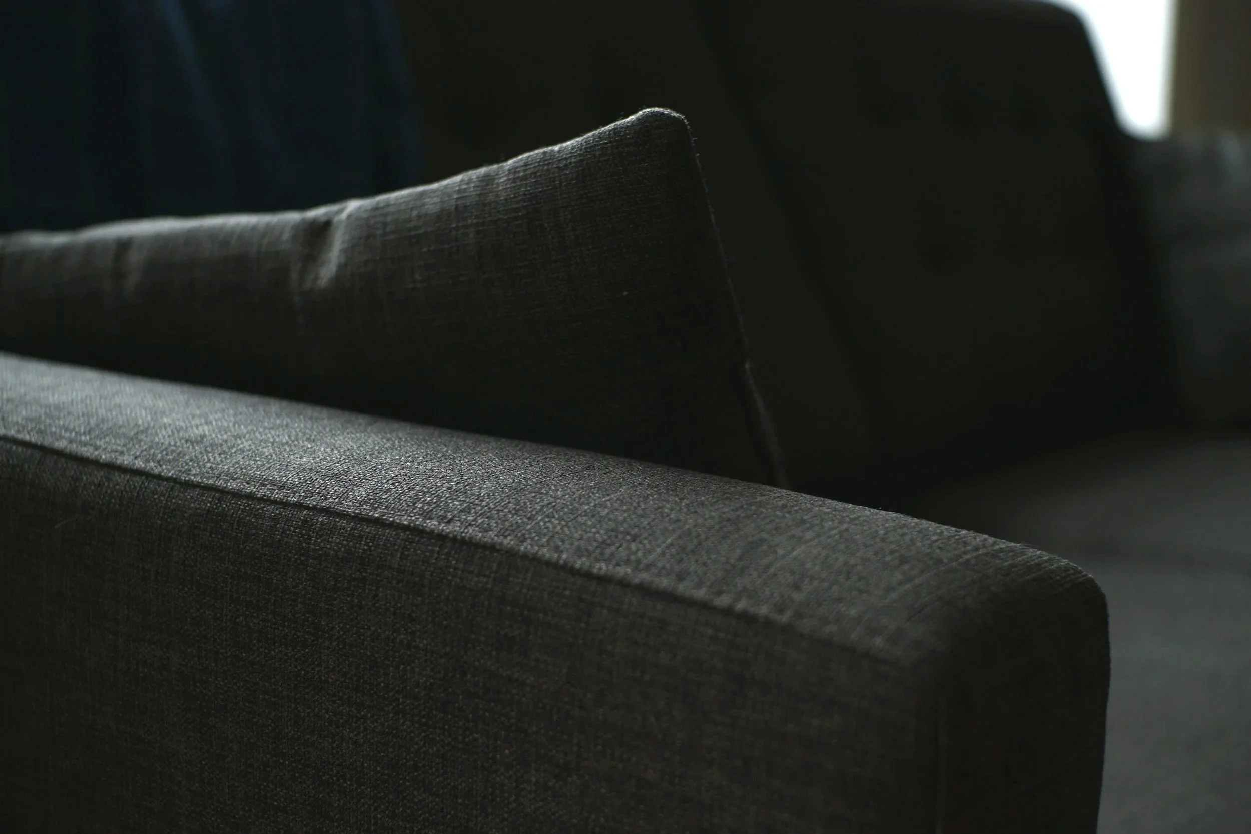 Close-up of a dark gray upholstered chair with textured fabric, illuminated by soft light.