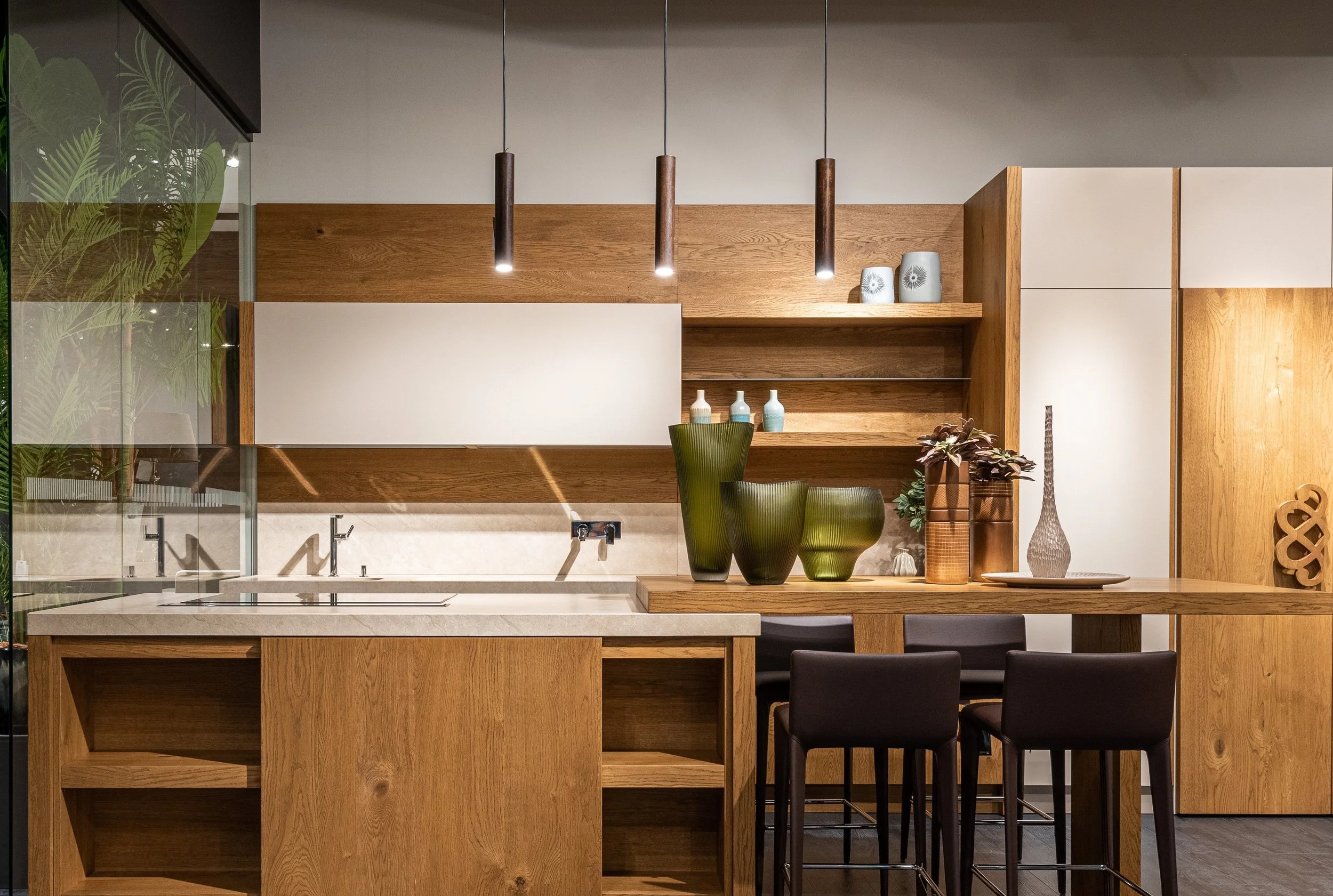 Modern kitchen with wooden cabinets, a white countertop, and decorative vases and plants on a wooden shelf.
