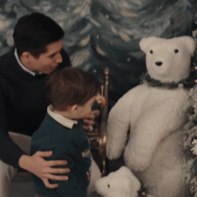 Un hombre y un niño observan un oso de peluche gigante en un entorno decorado con temática invernal.
