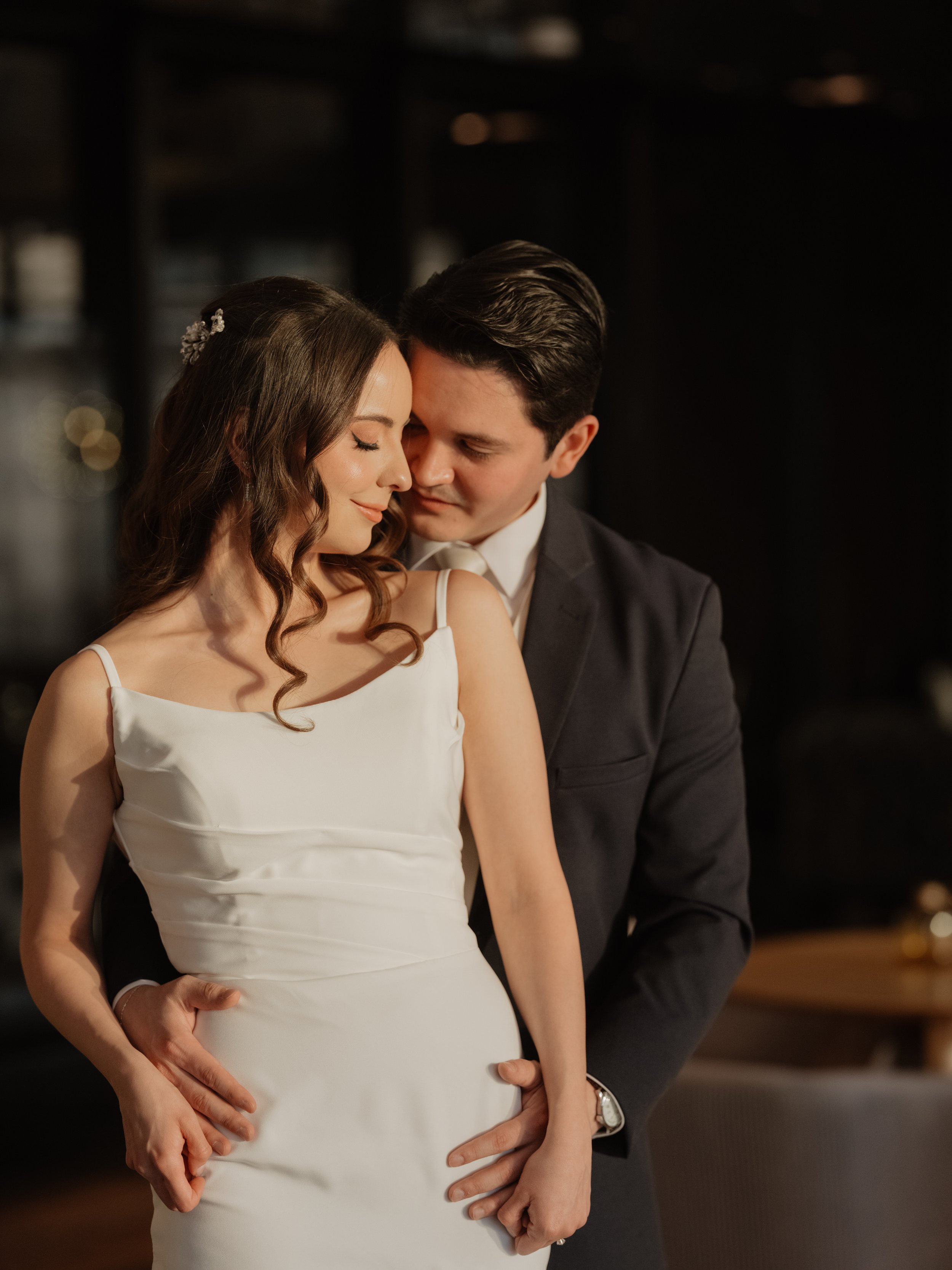 Pareja romántica en una pose íntima en un entorno oscuro, con mujer de vestido blanco y hombre de saco oscuro.