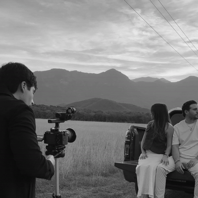 Un grupo de personas filmando en un campo con montañas de fondo, en un día nublado, en blanco y negro.