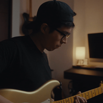 Joven tocando una guitarra eléctrica en una habitación con iluminación tenue.