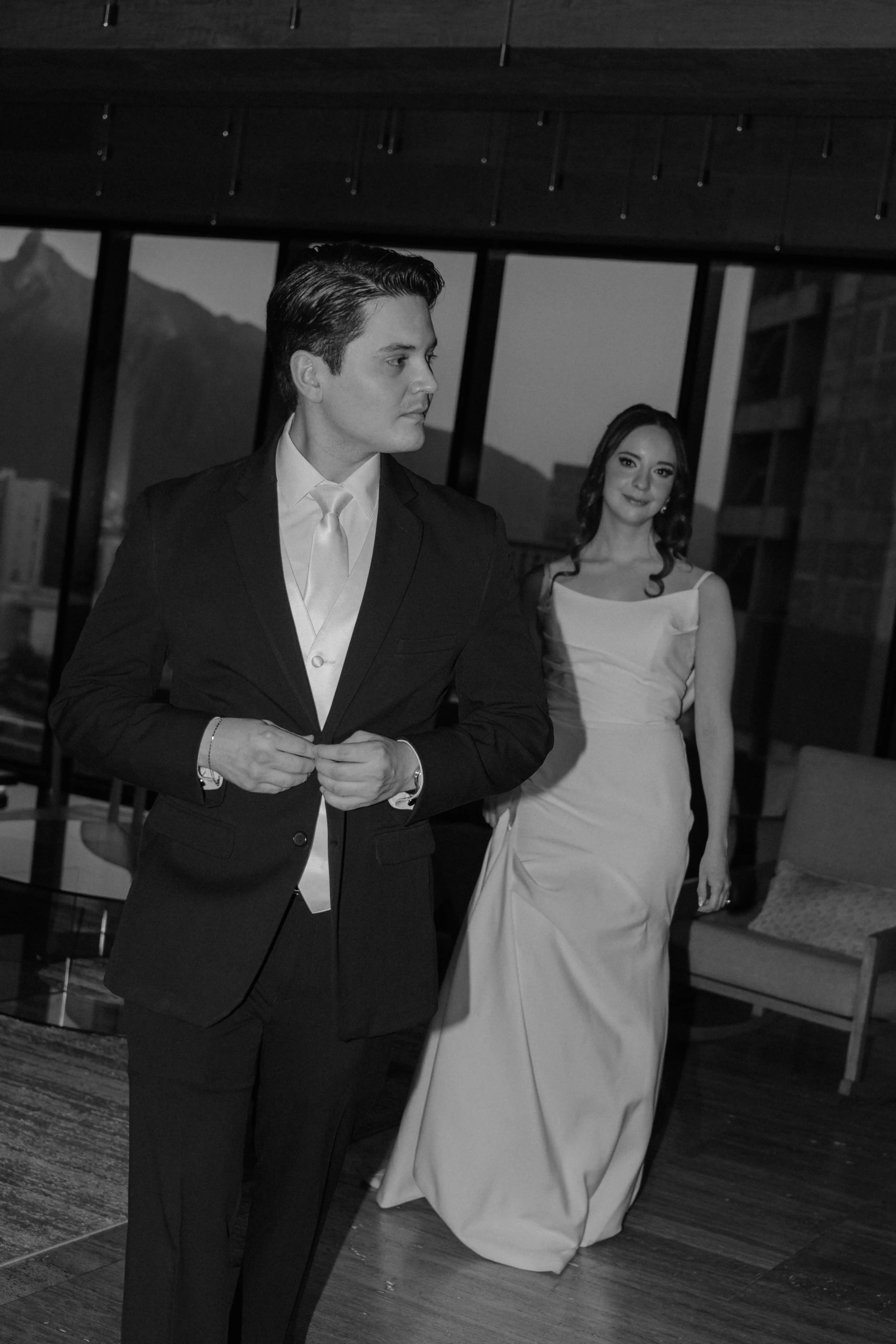 Pareja en ropa formal en un interior moderno, con vistas a montañas a través de ventanas grandes.