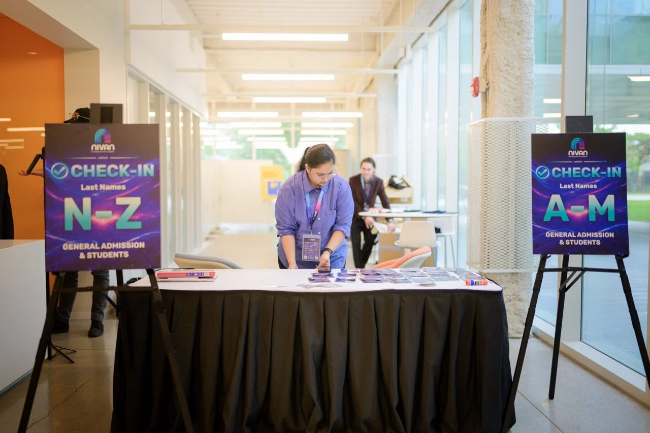 Registration table at a conference or event with check-in signs for last names N-Z and A-M, and staff preparing materials in a bright, modern lobby area.