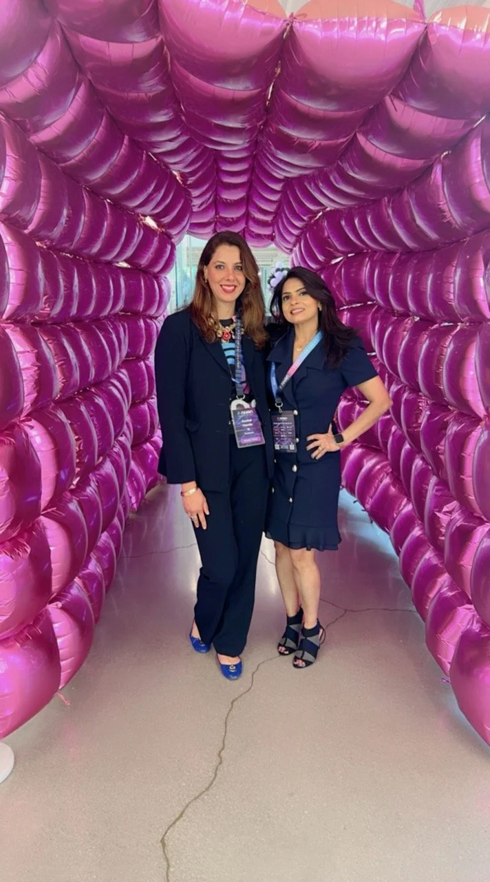 Two women standing inside a pink balloon tunnel, smiling at the camera.