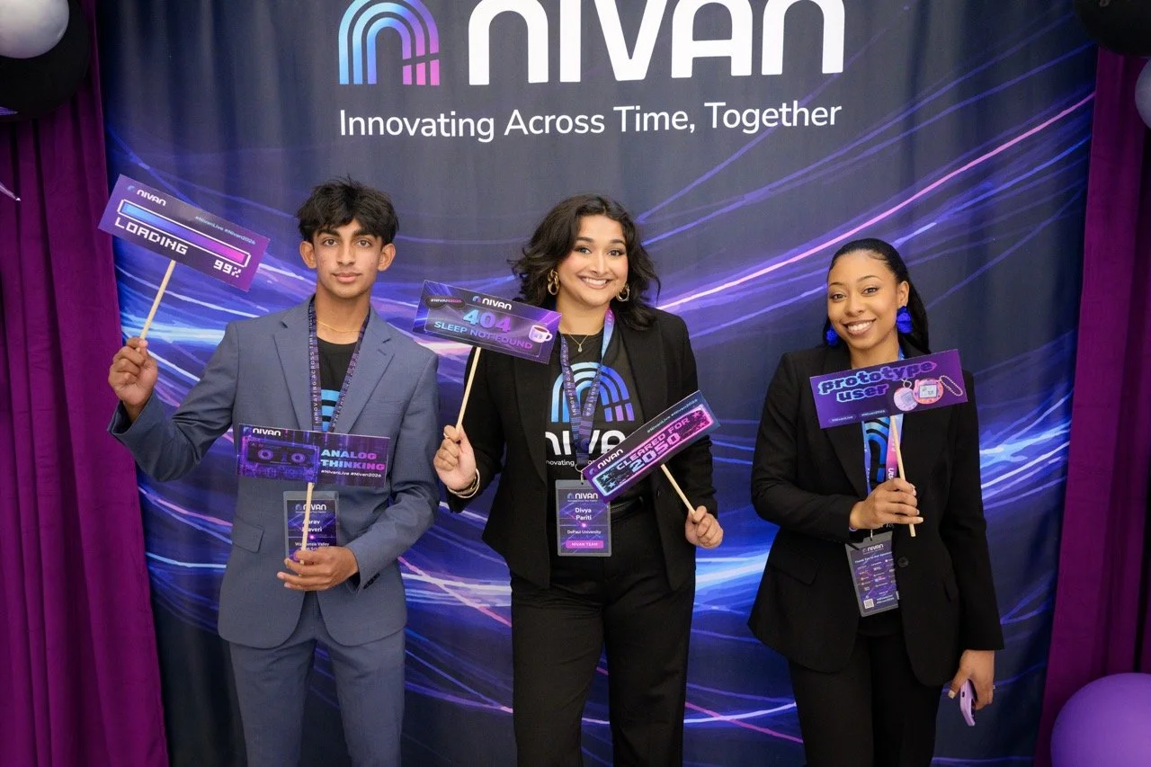 Three people standing in front of a Nivan display holding colorful signs with tech-related messages at a conference or event.