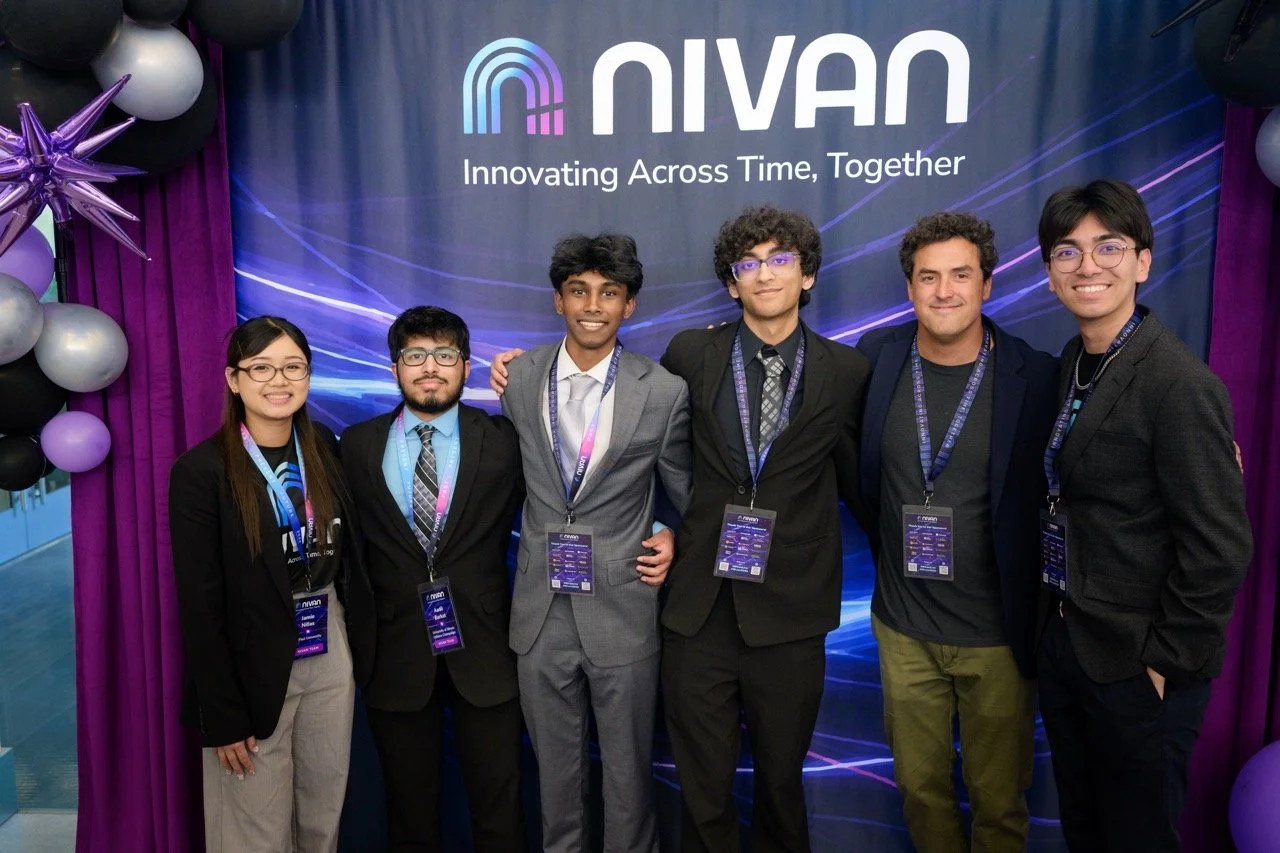 Six young professionals standing in front of a Nivan booth with balloons and purple curtains at a conference, smiling for the camera.