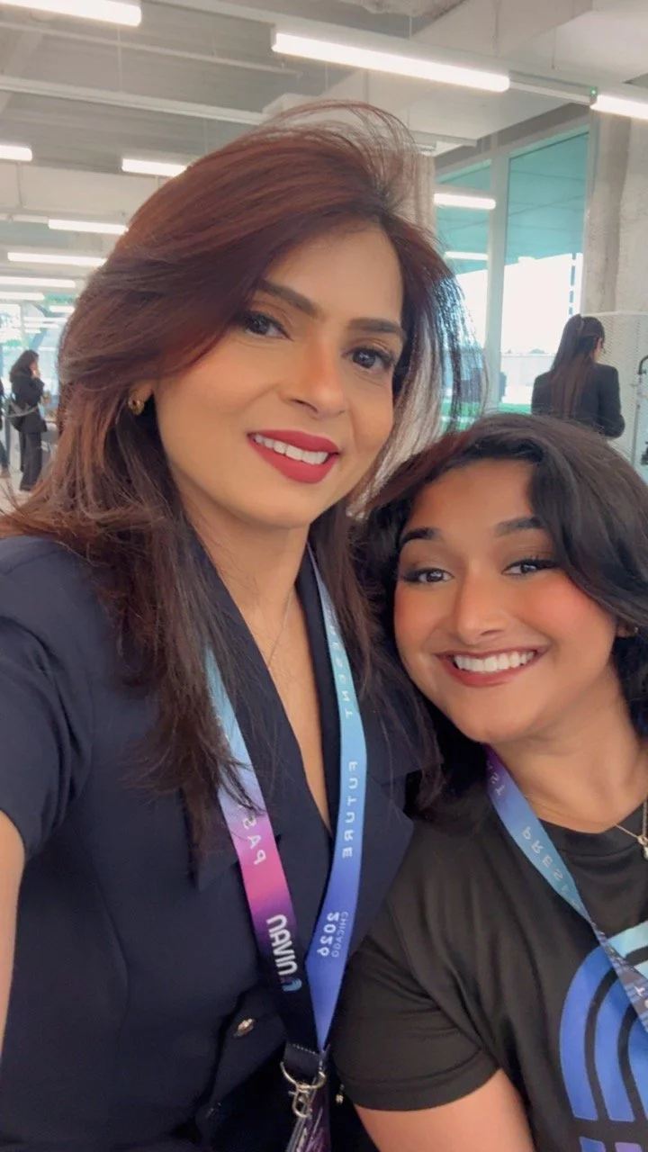 Two women smiling for a selfie at an indoor event with conference badges hanging around their necks.
