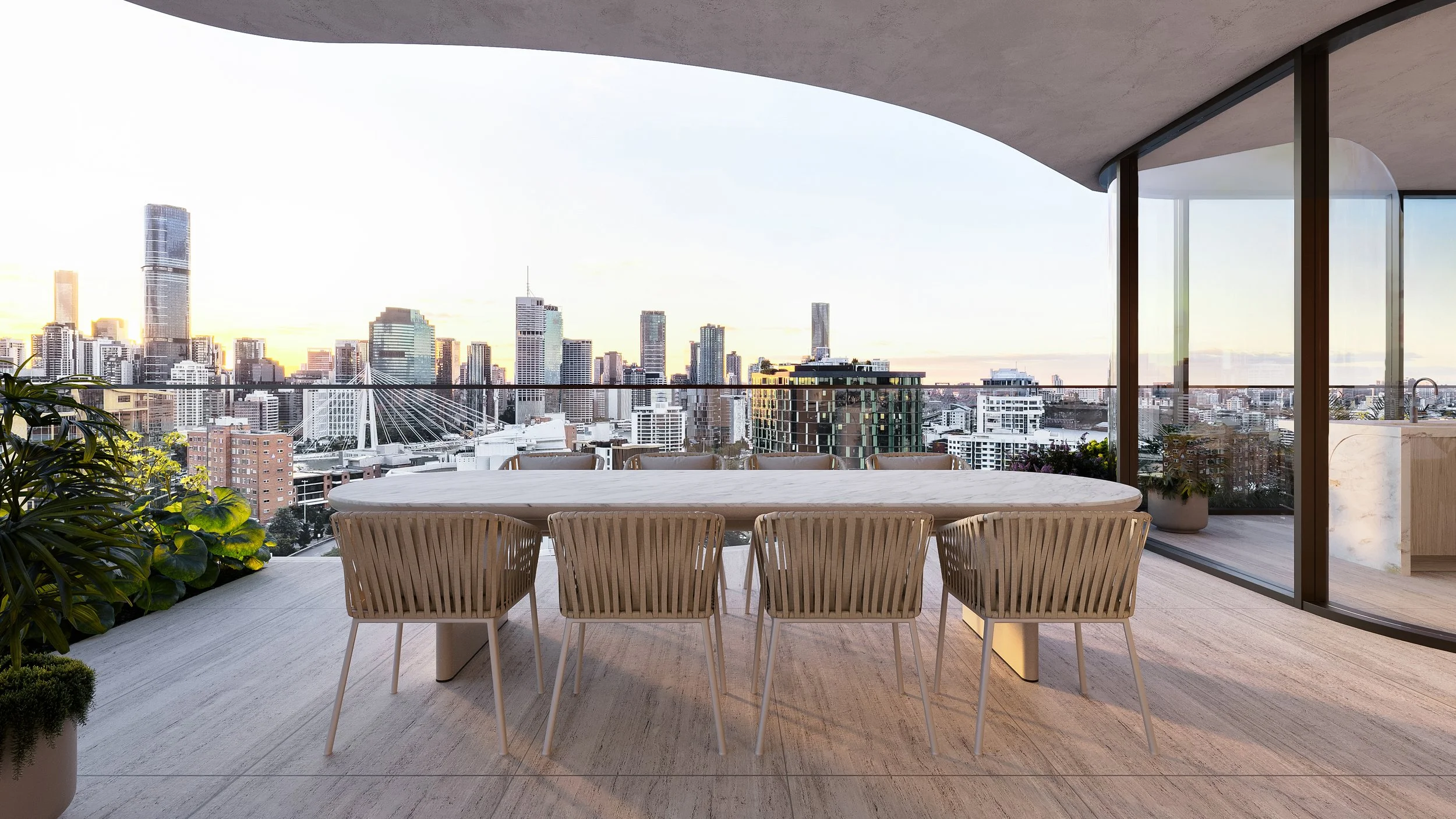 Banksia Kangaroo Point. Joe Adsett Designed. Modern balcony with a round dining table and woven chairs overlooking a city skyline at sunset, with glass railings and potted plants.
