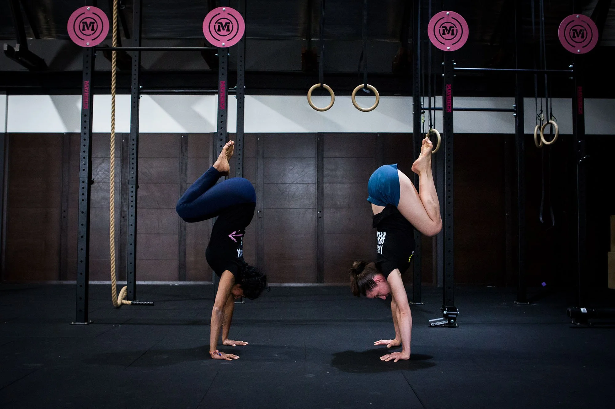 Two women in athletic clothing performing a tuck handstand in a gym