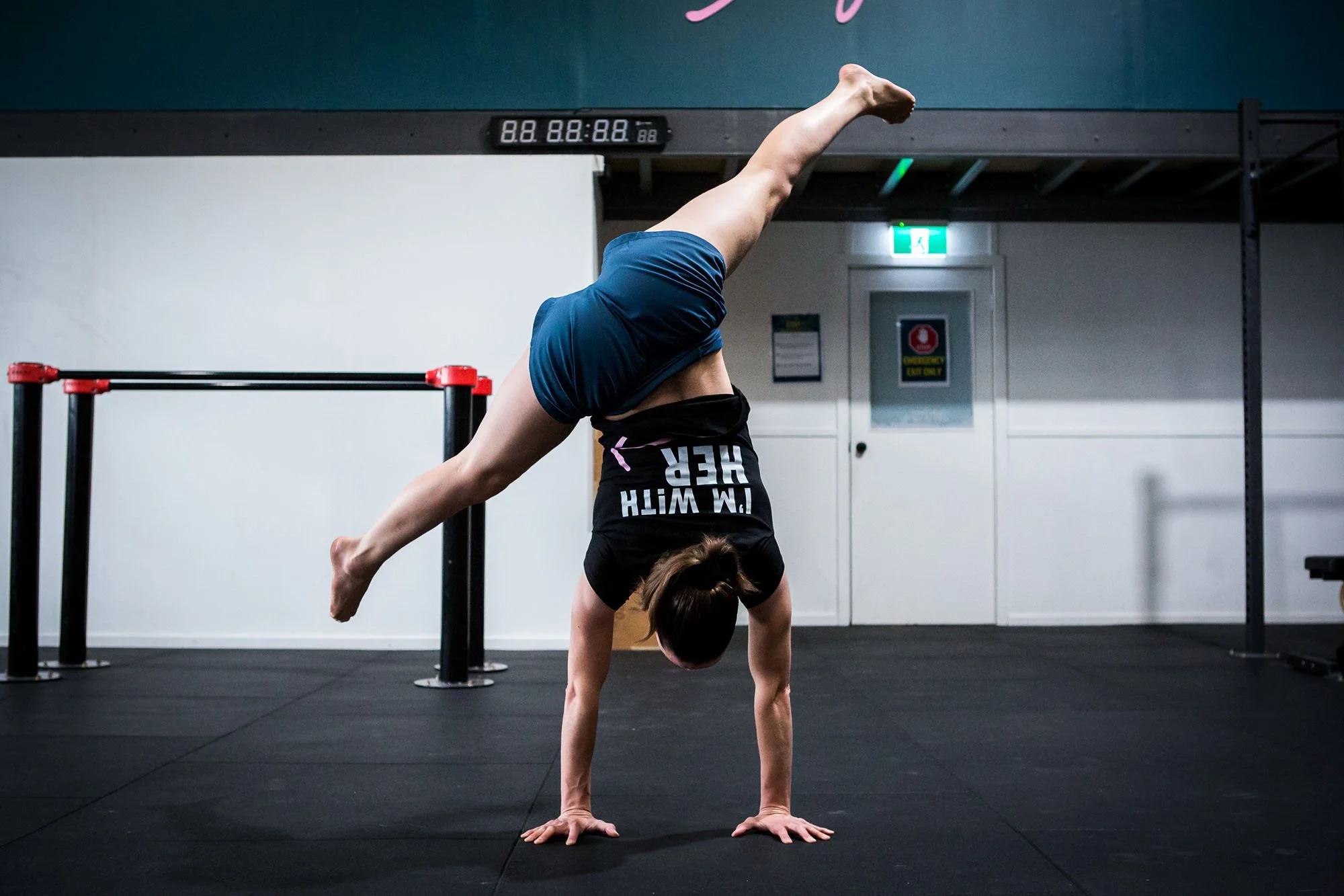 A woman is performing a handstand in a gym, with her legs extended in a split shape