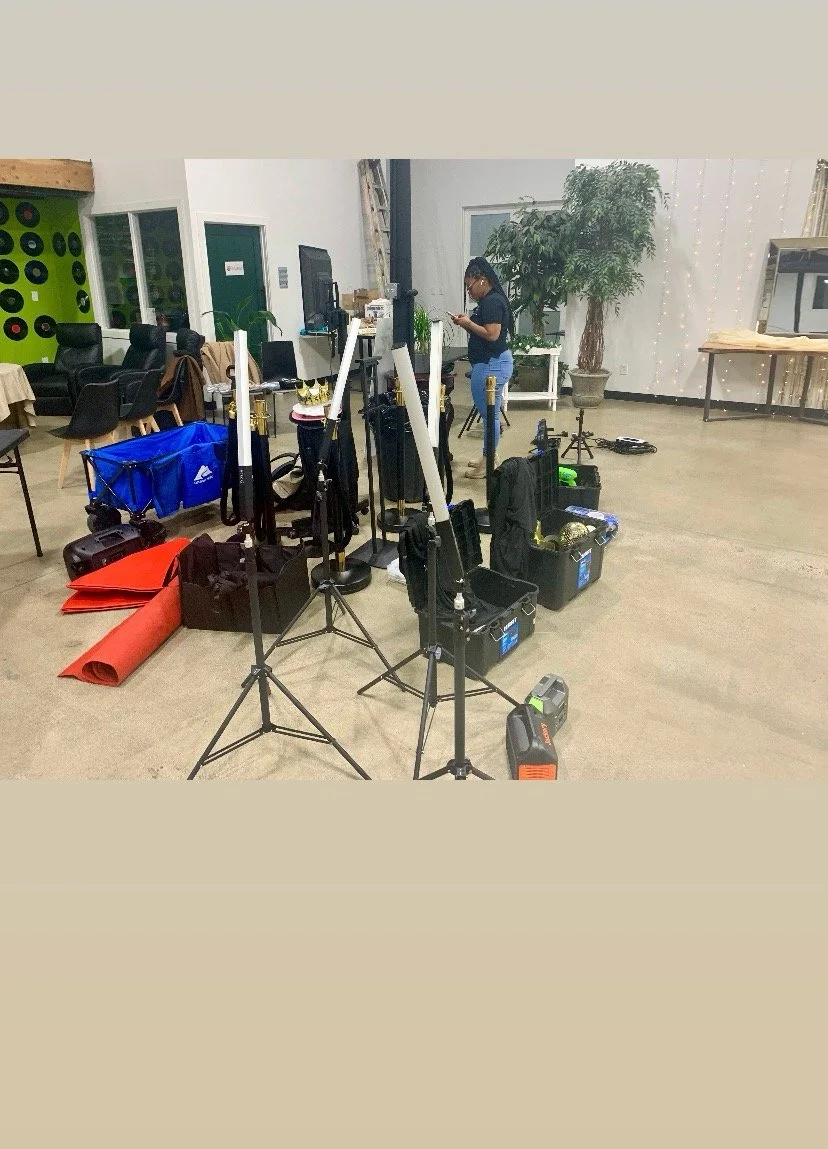 Setup for a photography or videography shoot with lighting equipment, tripods, and boxes in an indoor space with seating and plants.