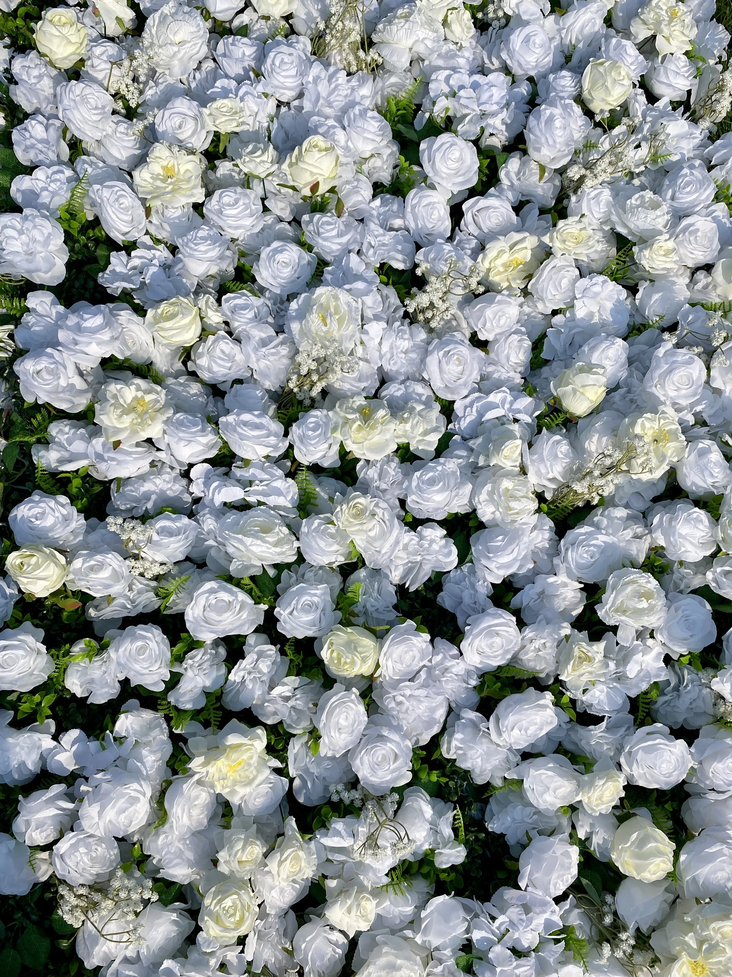 A dense arrangement of white roses, some fully bloomed and others in bud, with green leaves and small white filler flowers.