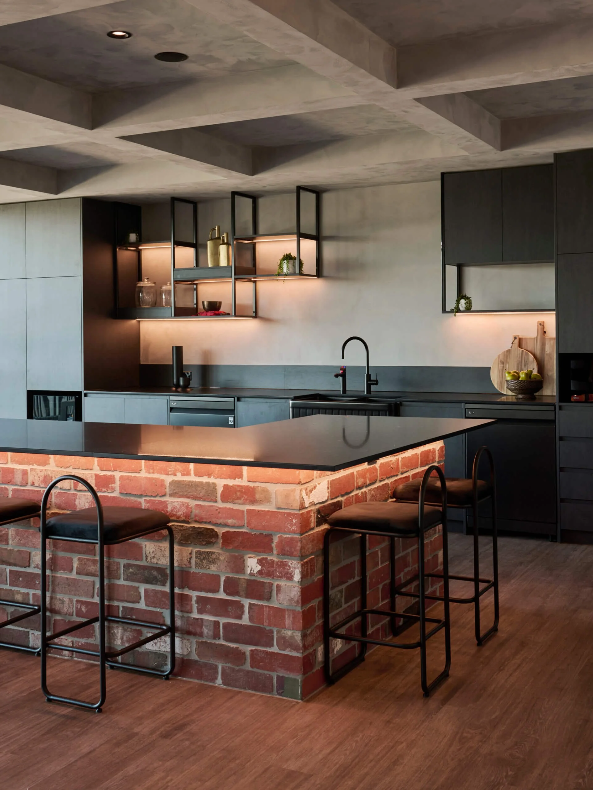 Modern kitchen with black cabinets, brick island, and open metal shelves with decorative items, including vases and bowls.