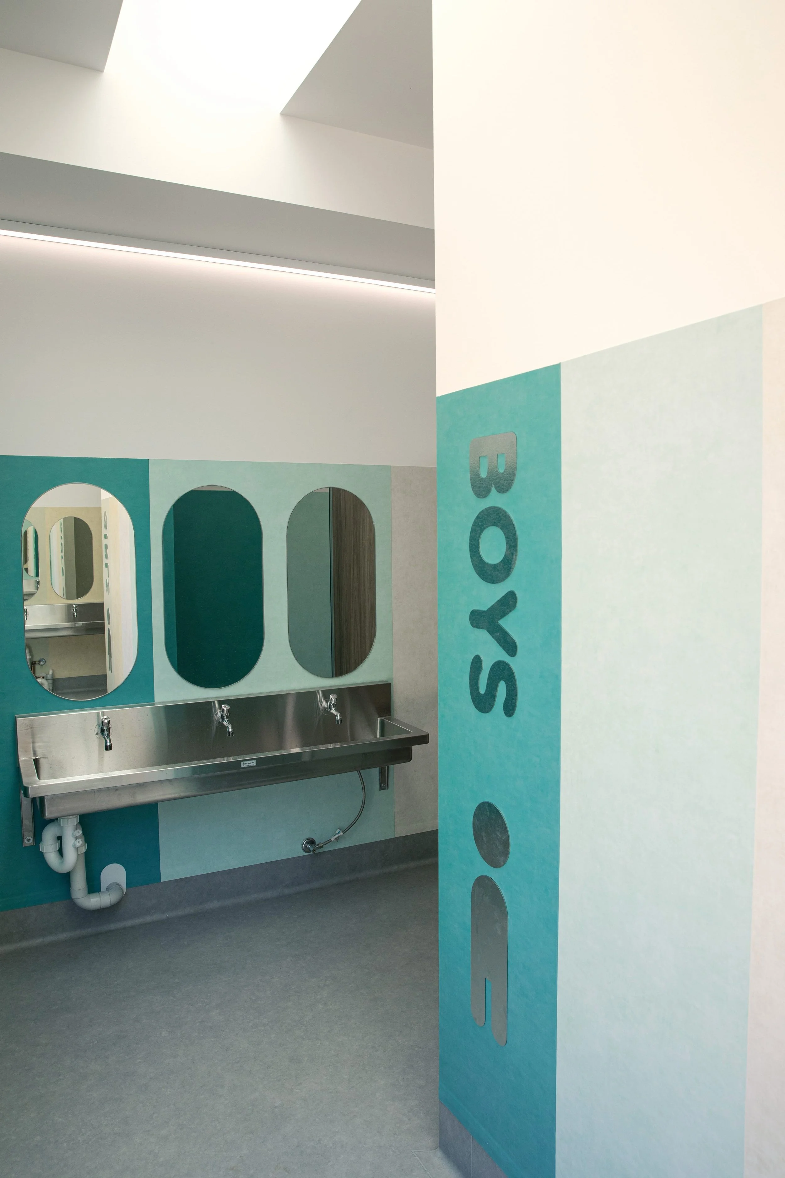 School bathroom with a stainless steel sink, three oval mirrors, and blue and gray decorated walls.