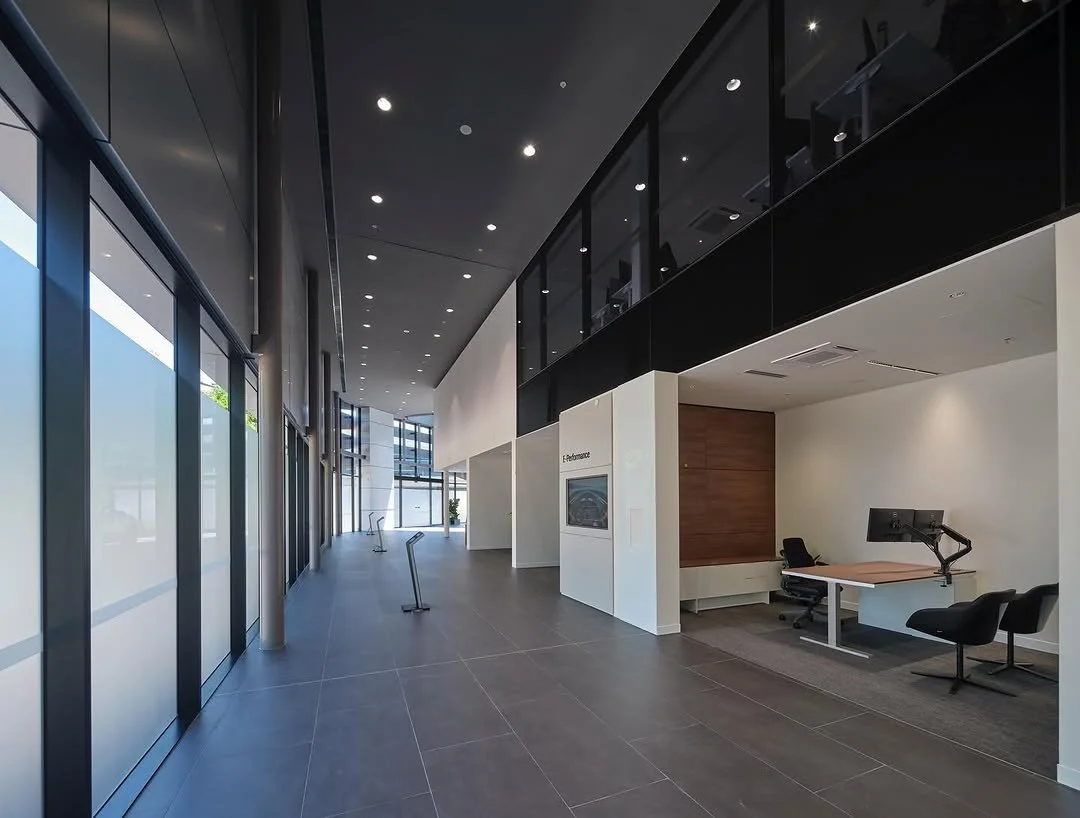 Modern commercial office interior with glass doors, a reception area, and an upper balcony with glass railing.