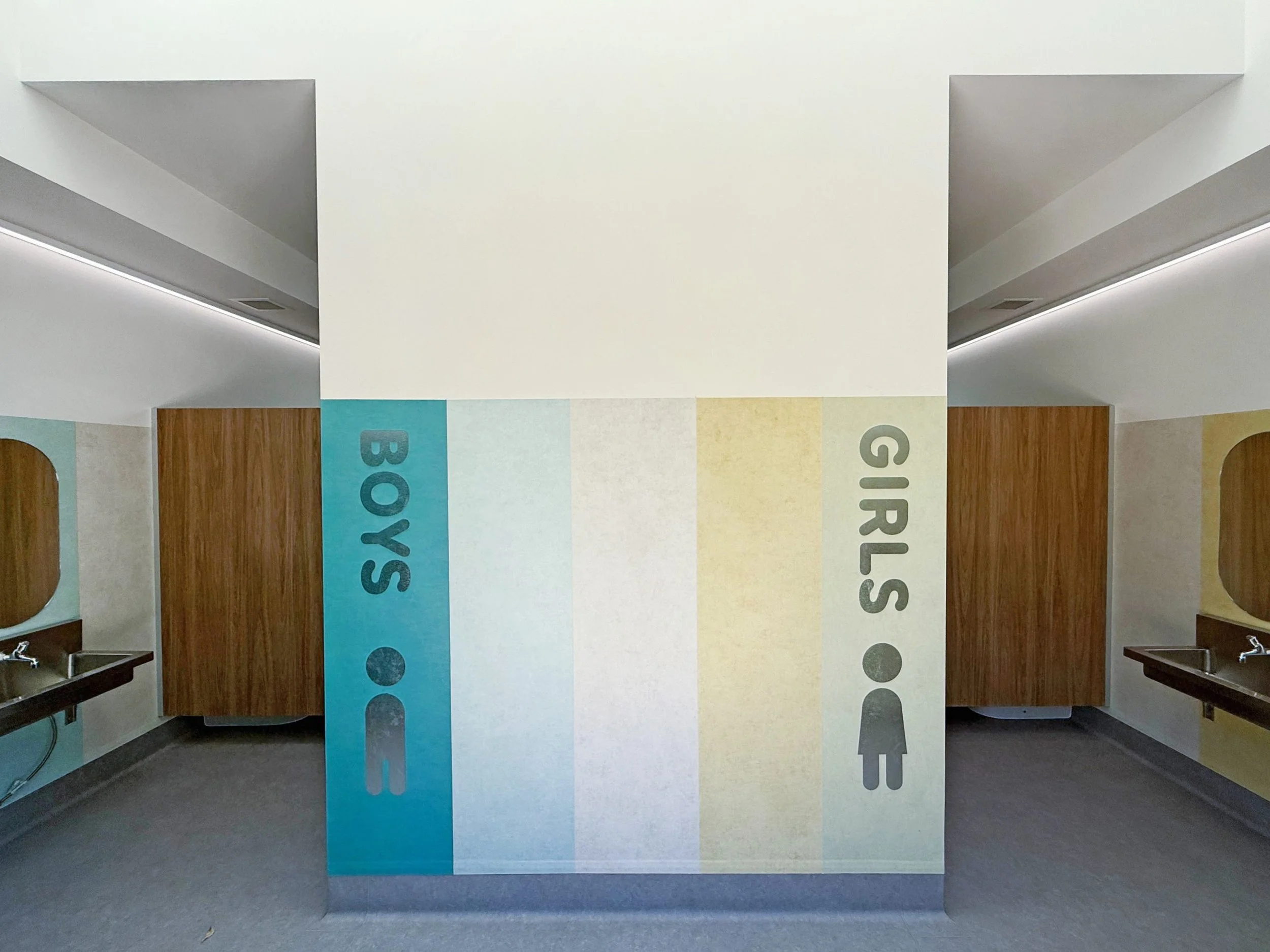 Public bathroom with colorful banners hanging from the ceiling, displaying letters B, O, S, G, I, R, and U, with sinks visible on each side.