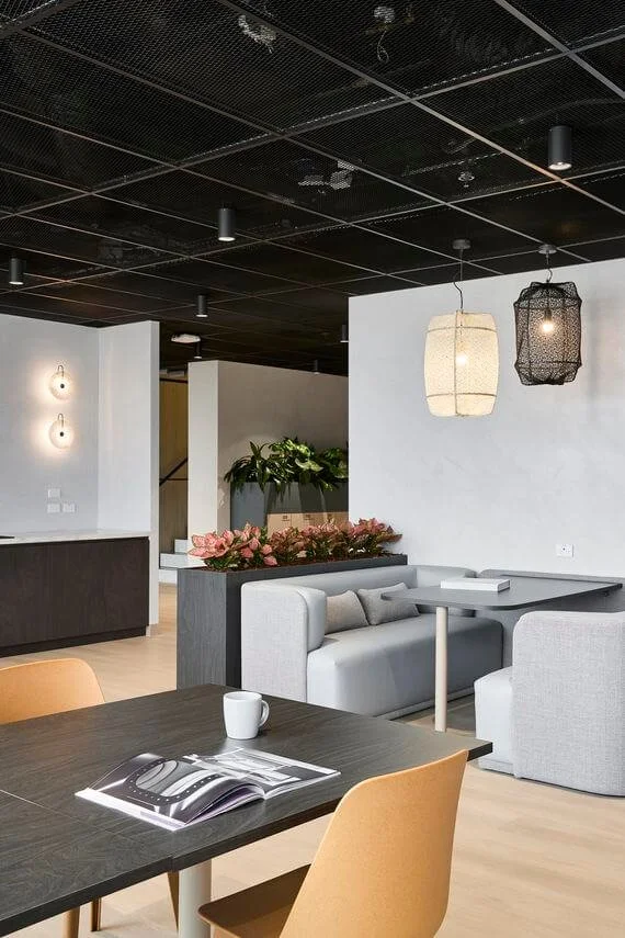 Modern dining area with a black table, beige chairs, a white sofa, and hanging light fixtures in a bright, stylish interior.