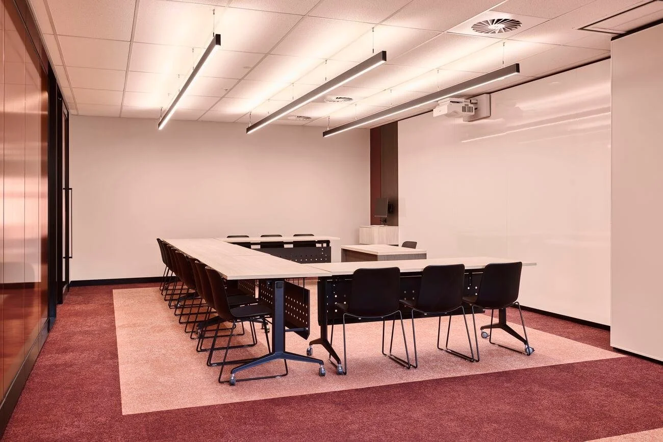 Empty conference room with U-shaped table, black chairs, white walls, and ceiling lights.
