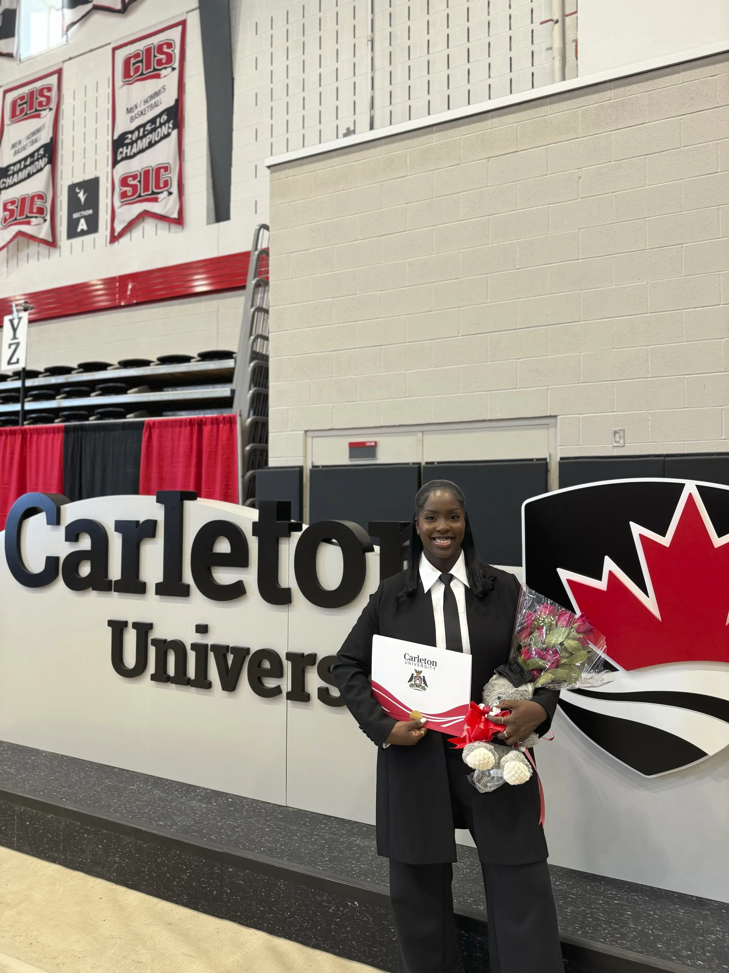 Smiling young woman holding a bouquet of flowers and an acceptance letter at Carleton University campus, standing in front of the Carleton University sign and a large Ontario Maple Leaf symbol.